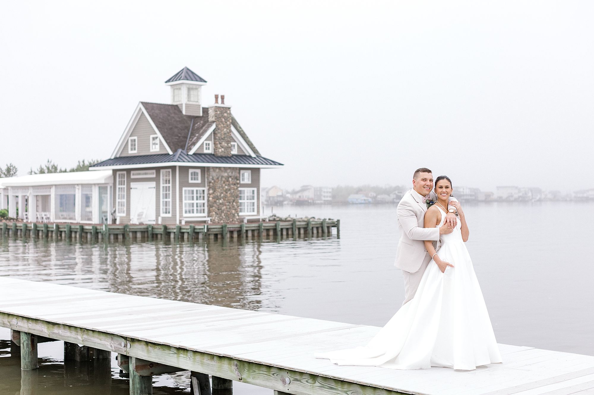 groom hugs bride from behind on dock in Manahawkin NJ