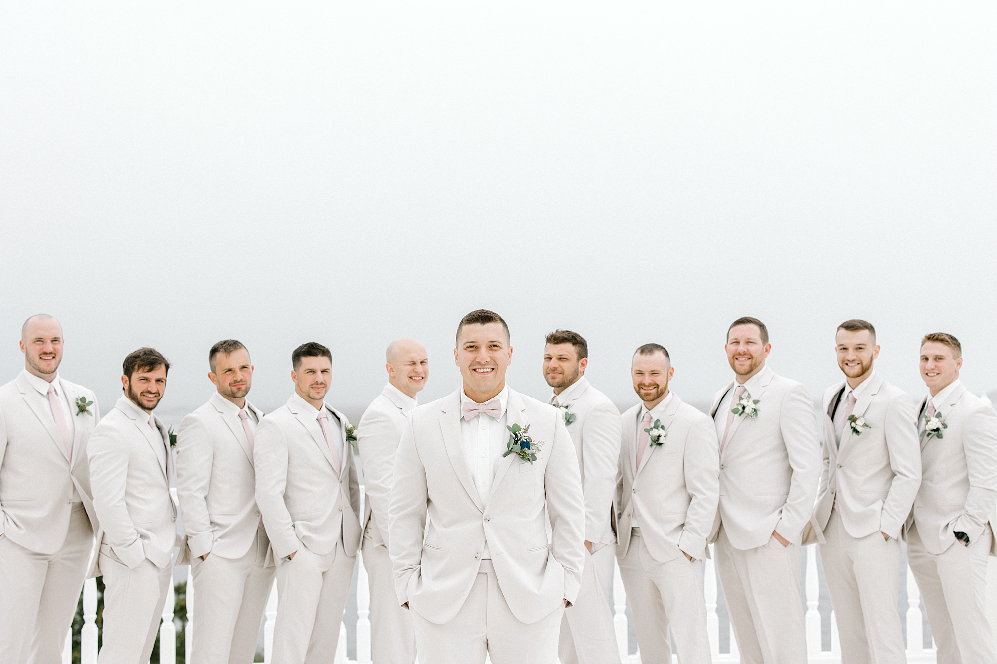 groom stands with groomsmen behind him in tusk suits