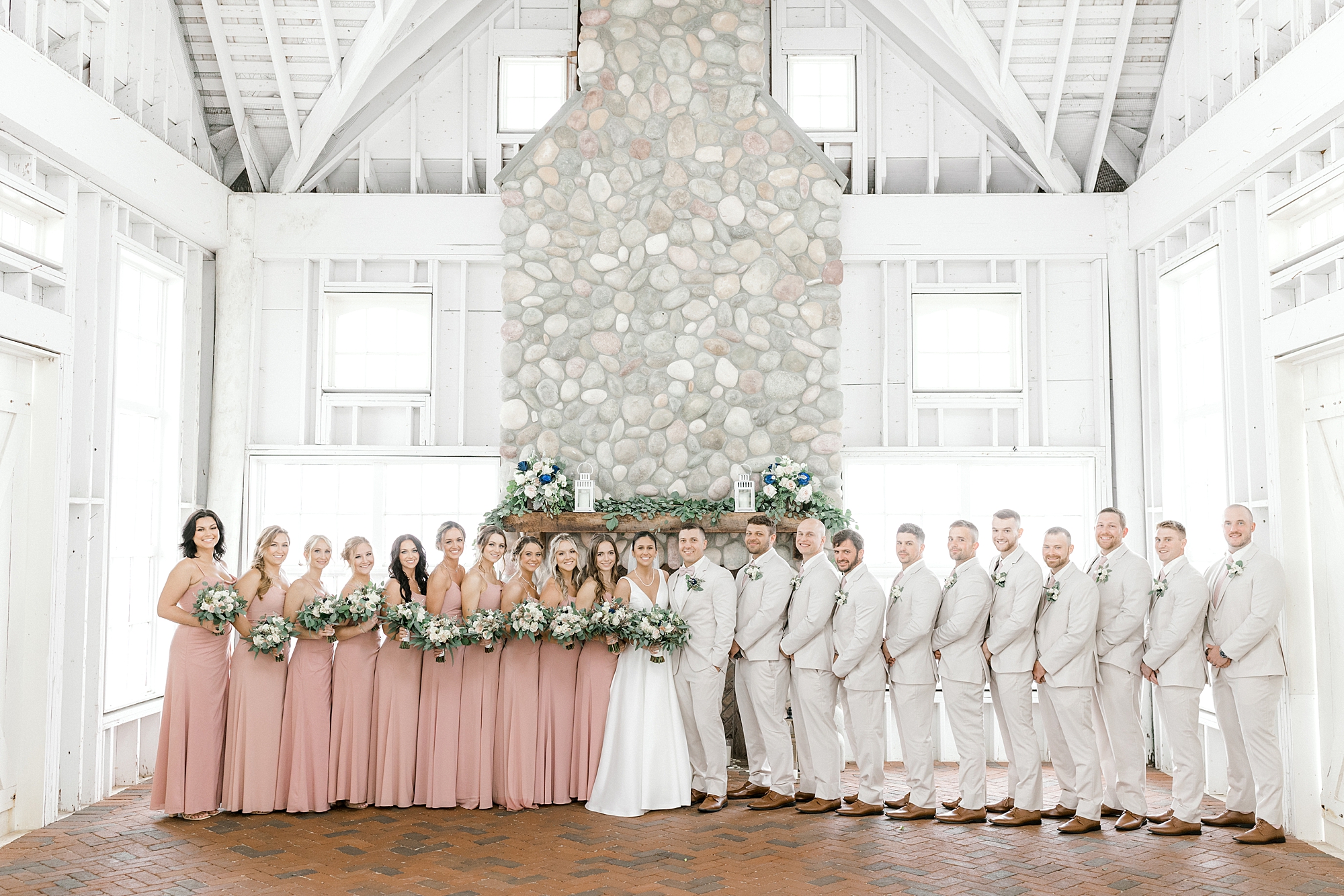 bride and groom stand with wedding party by stone fireplace inside Mallard Island Yacht Club