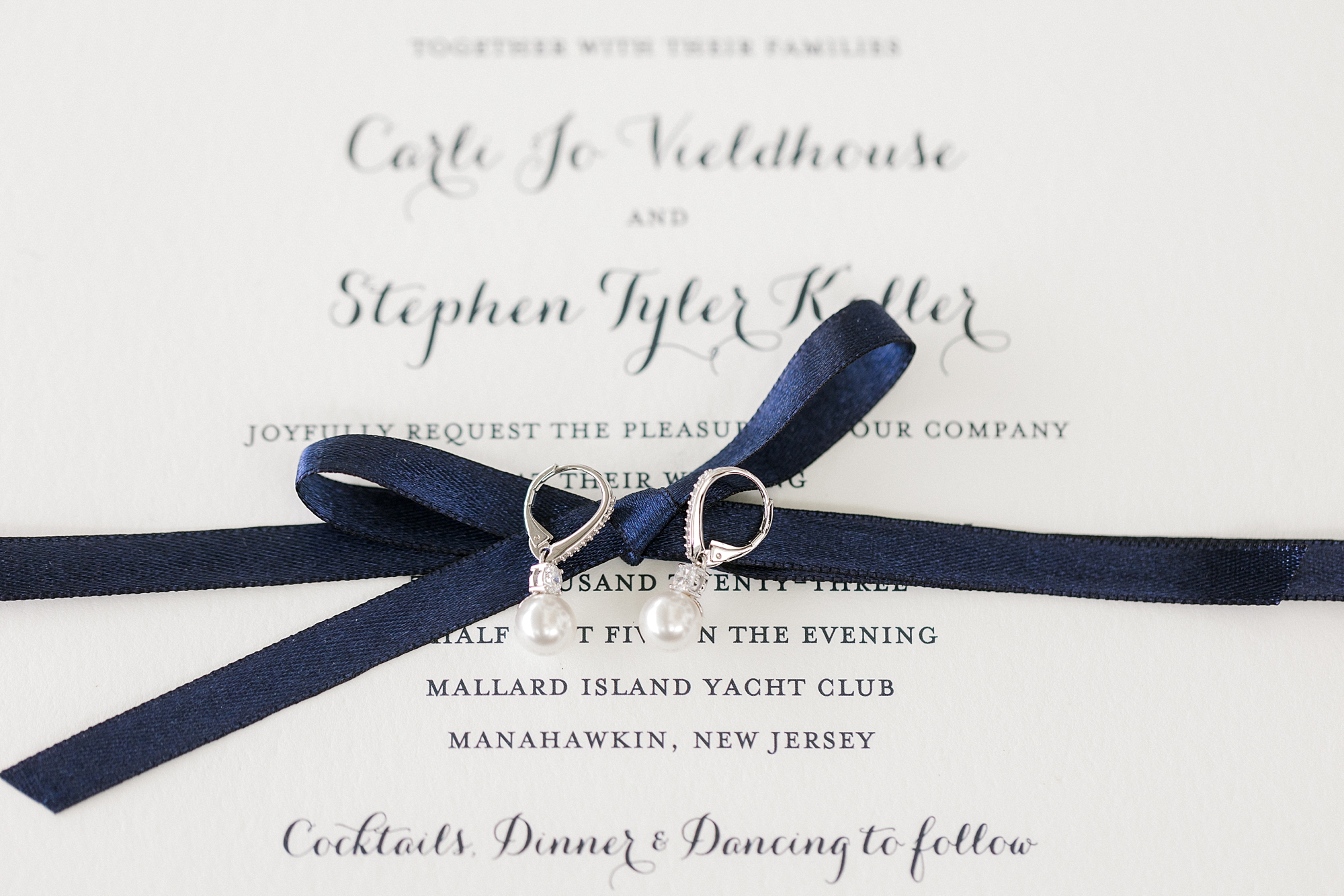 bride's diamond earrings rest on blue ribbon of invitation suite at Mallard Island Yacht Club