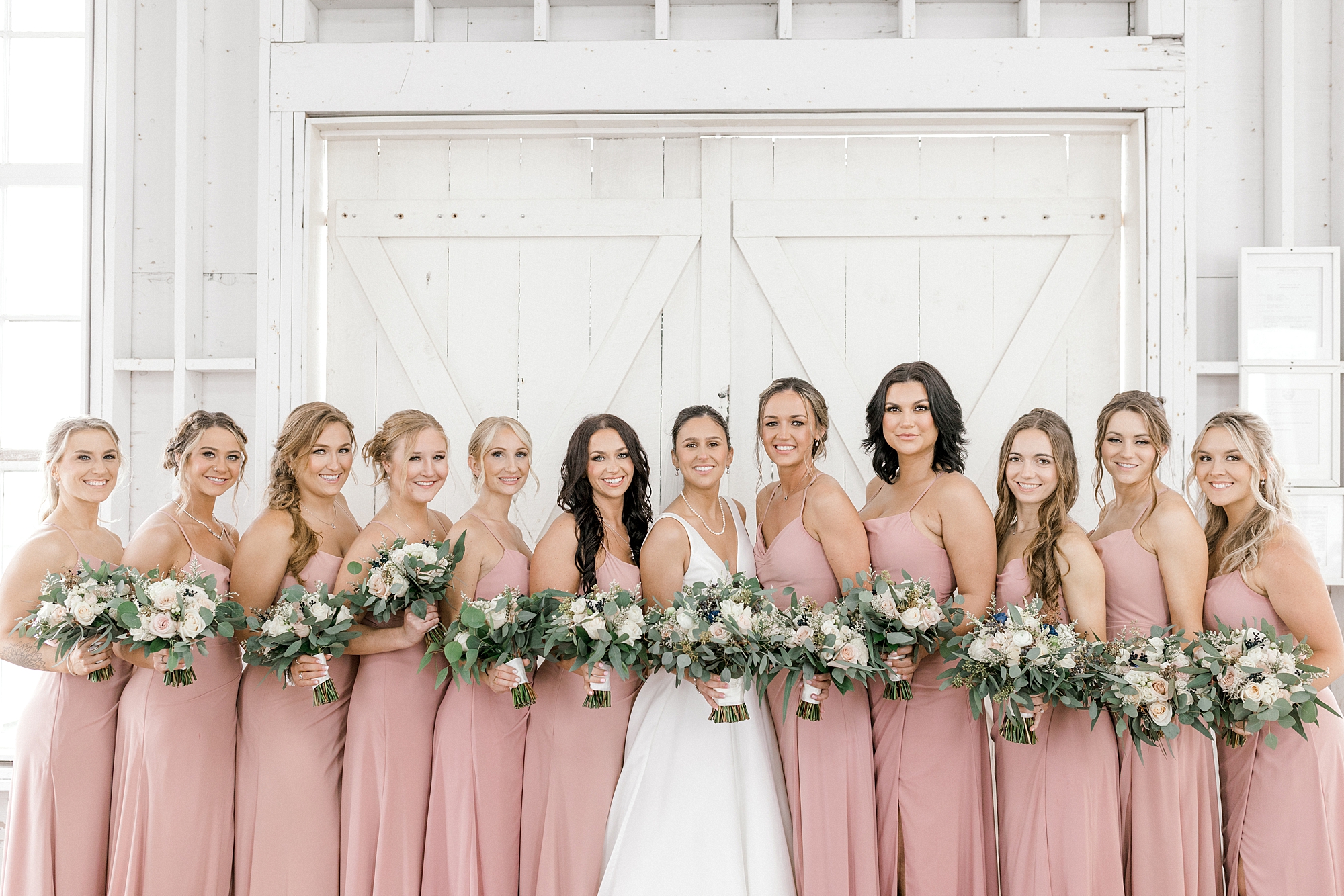 bride and bridesmaids stand together inside Mallard Island Yacht Club with dusty pink bridesmaid dresses