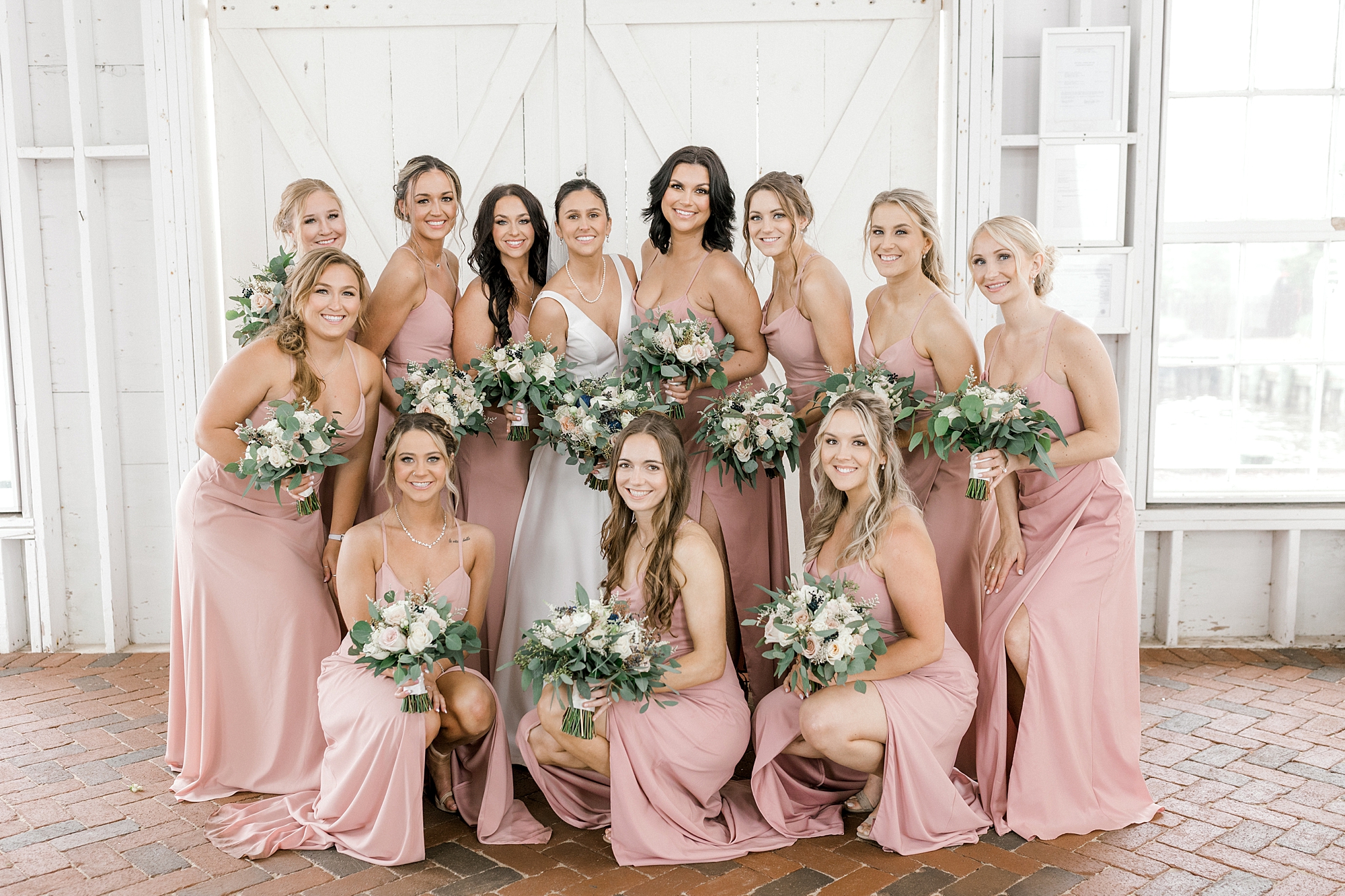 bride poses with bridesmaids in dusty pink gowns by stone fireplace at Mallard Island Yacht Club