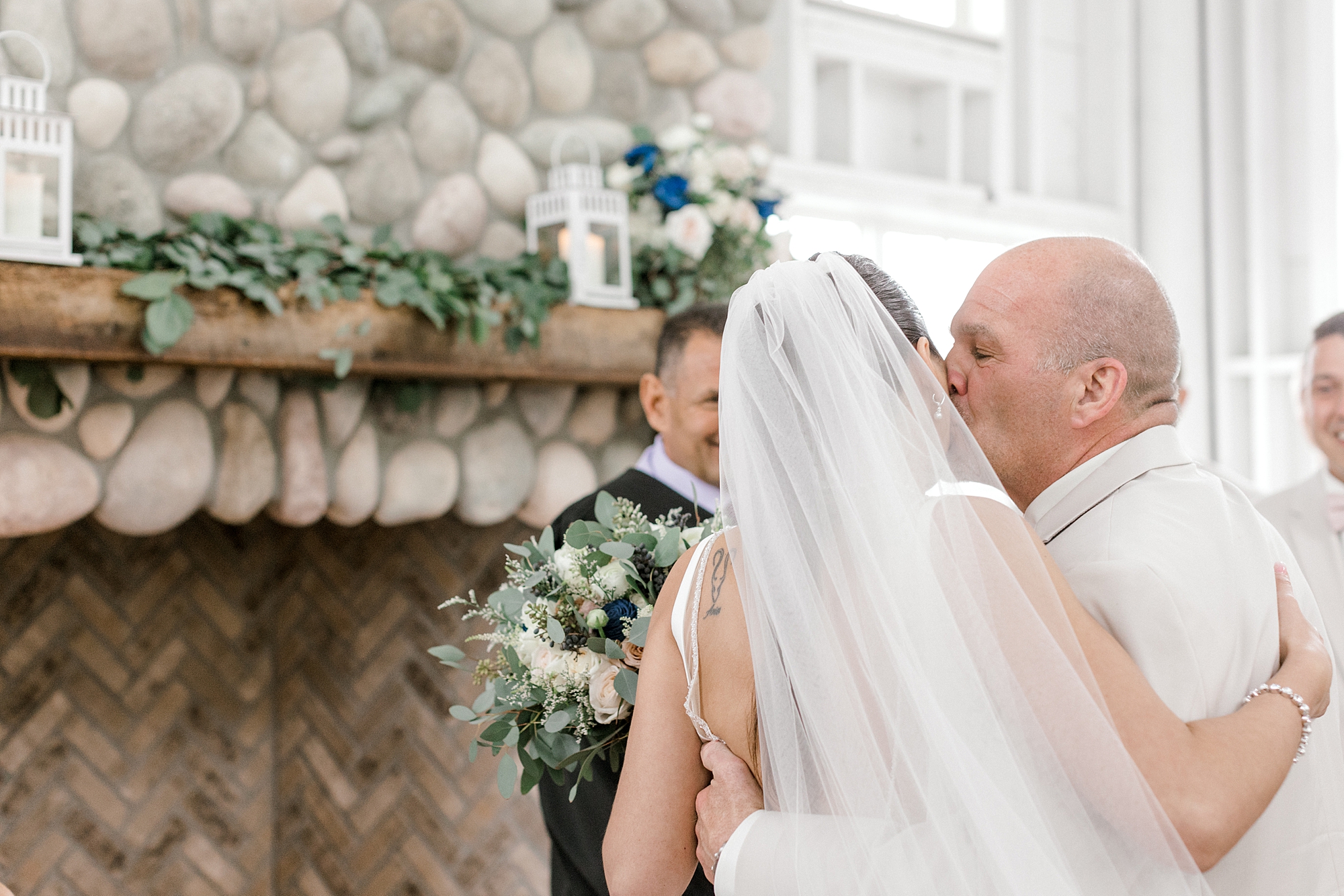 father kisses bride's cheek by fireplace at Mallard Island Yacht Club