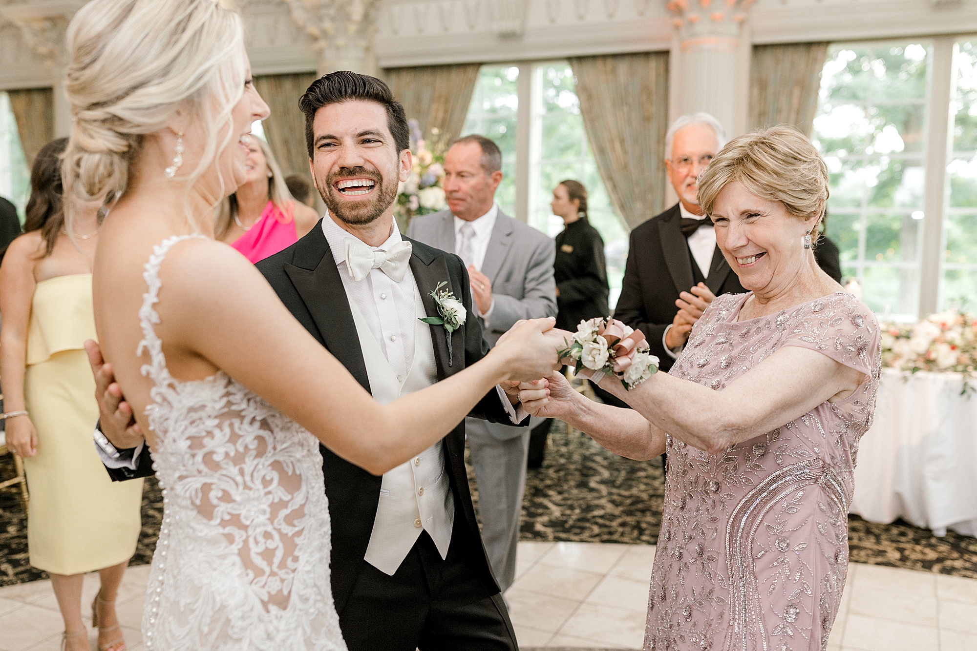 groom smiles at bride and mother dancing during during NJ wedding reception