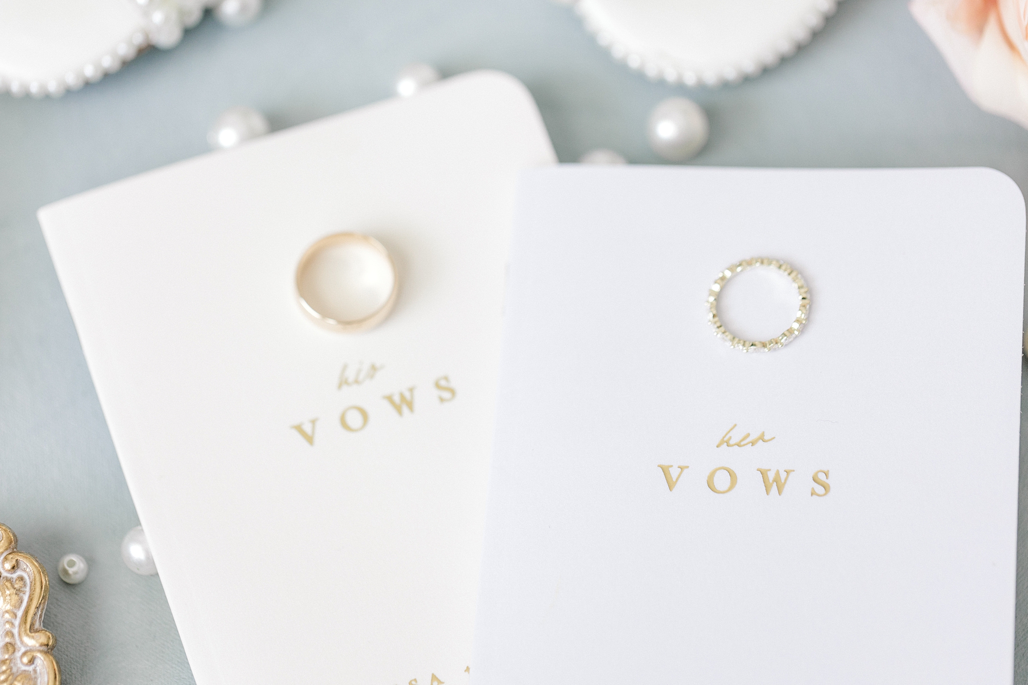 gold wedding rings lay on white vow booklets