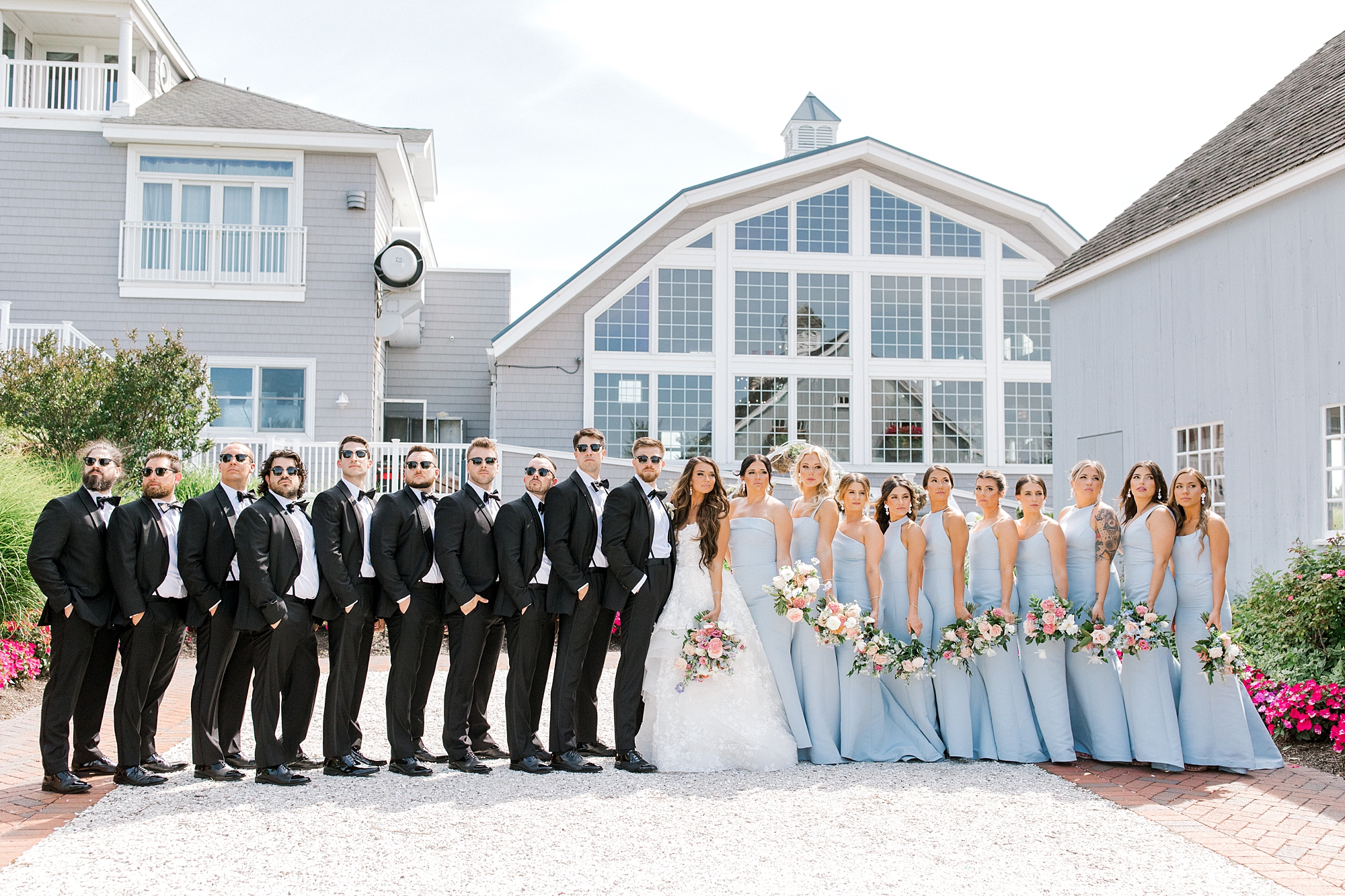 bride and groom hug with bridesmaids in blue dresses and groomsmen in black suits in front of Bonnet Island Estate