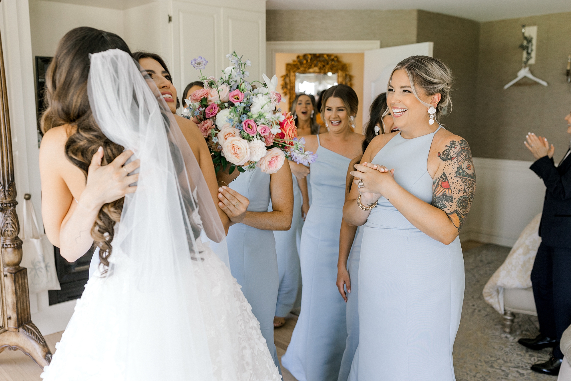 bride hugs bridesmaids in light blue gowns during first look