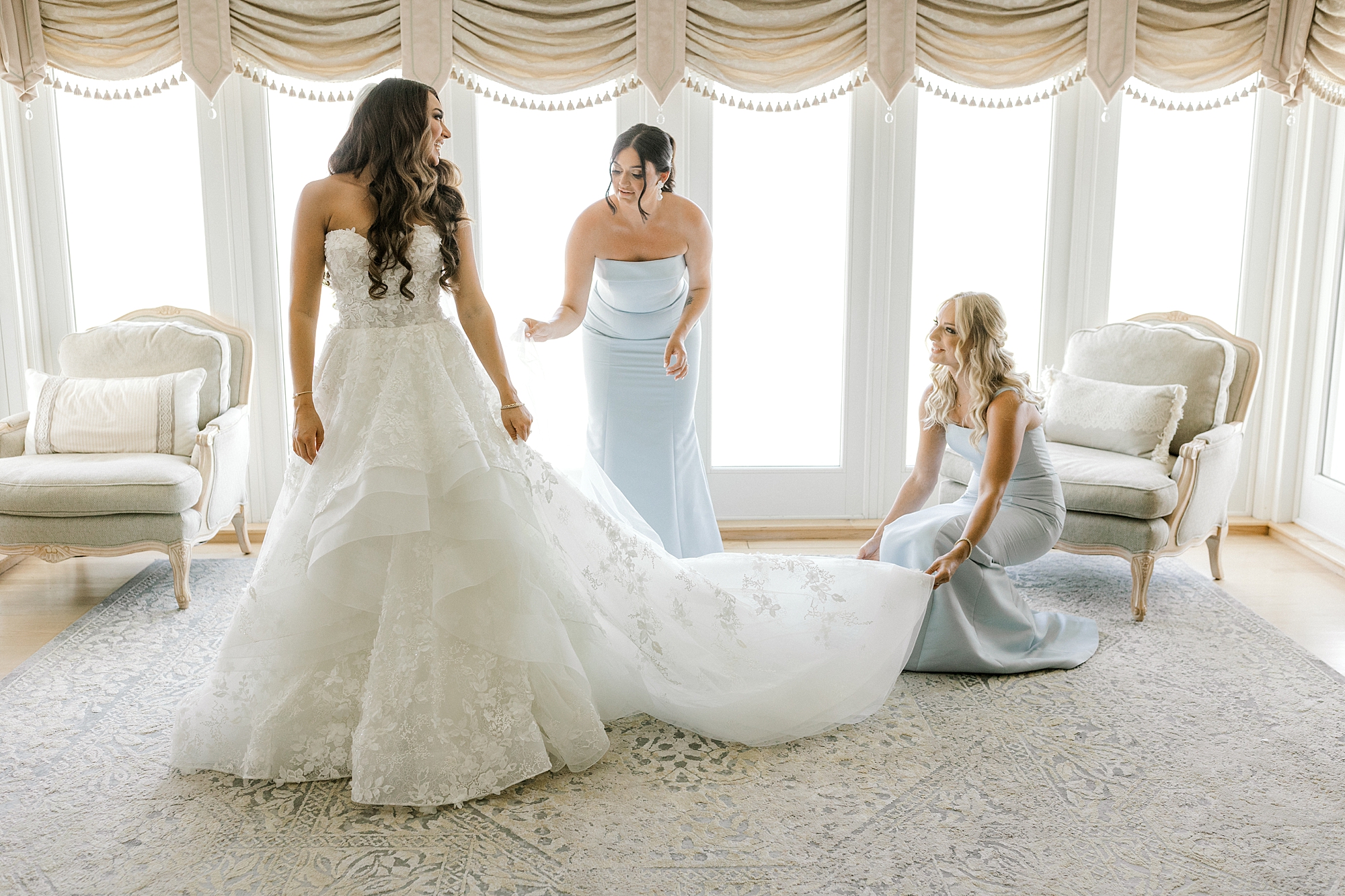 bridesmaids in blue gowns help bride with train in bridal suite in New Jersey
