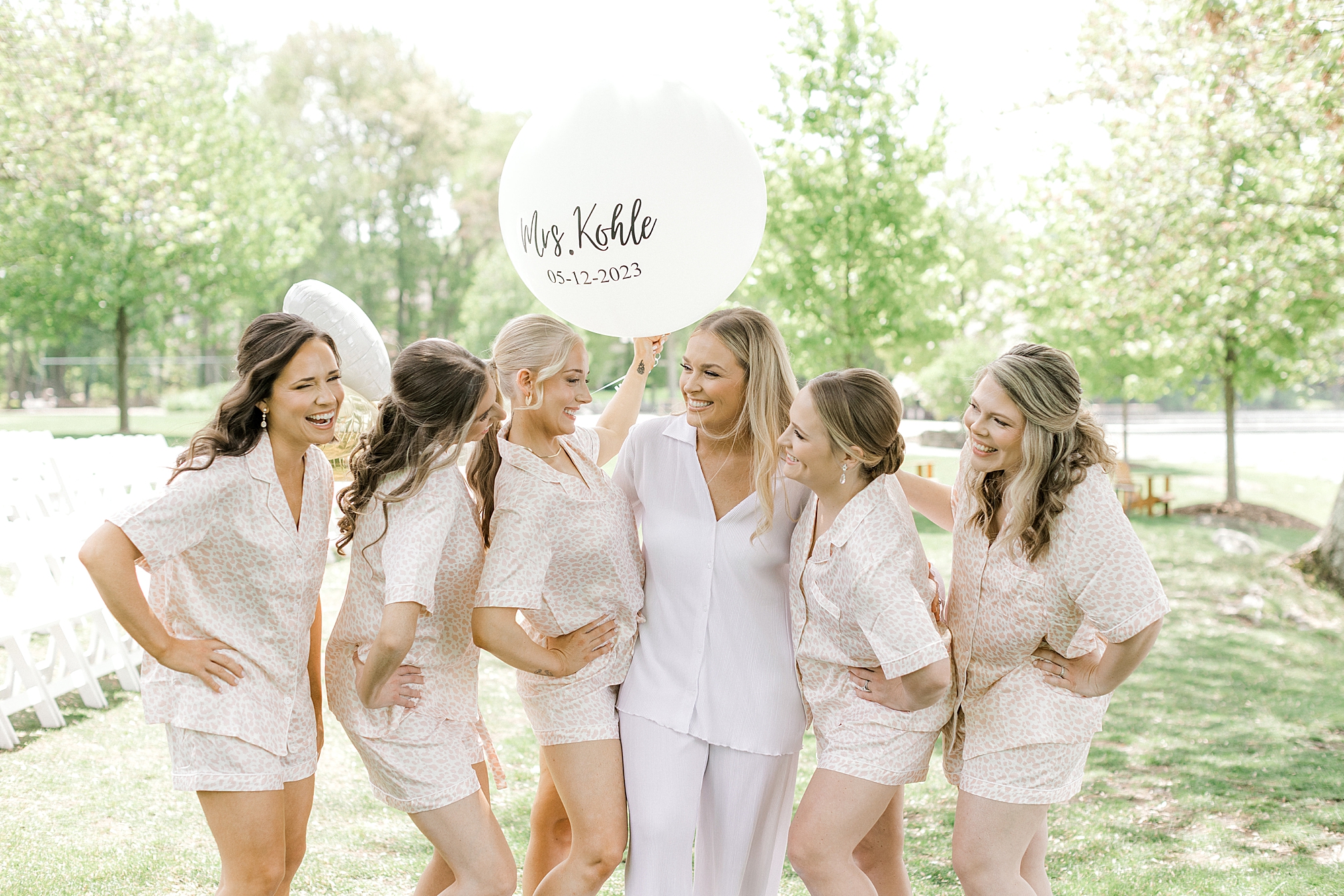 bride poses with bridesmaids in matching pajamas with custom balloon