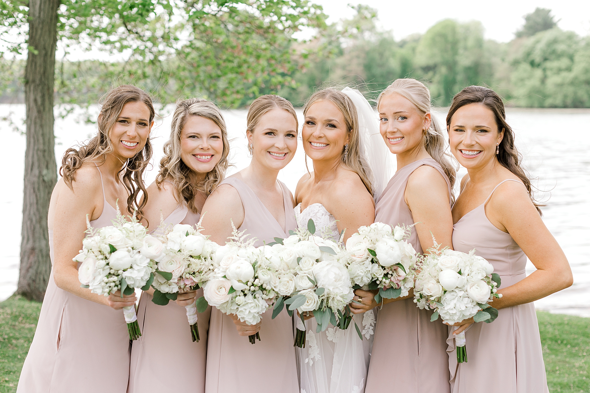 bride poses with bridesmaids in pink gowns and white flowers