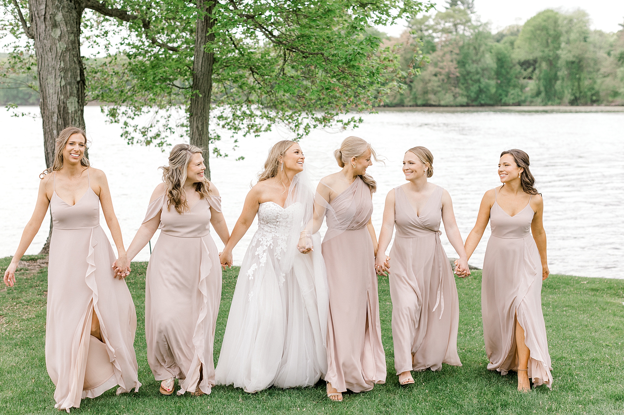 bride and bridesmaids hold hands walking up hill at Indian Trail Club