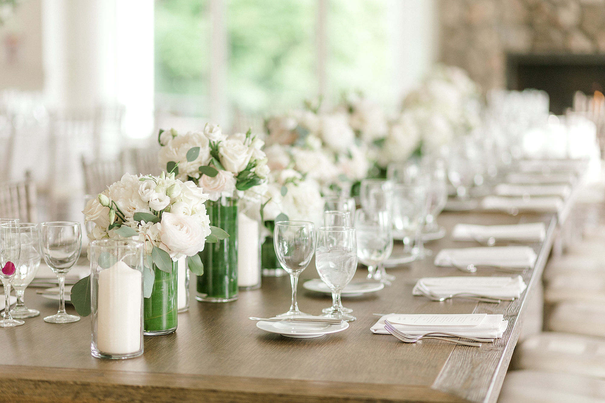 wedding reception with white roses and greenery down center of table