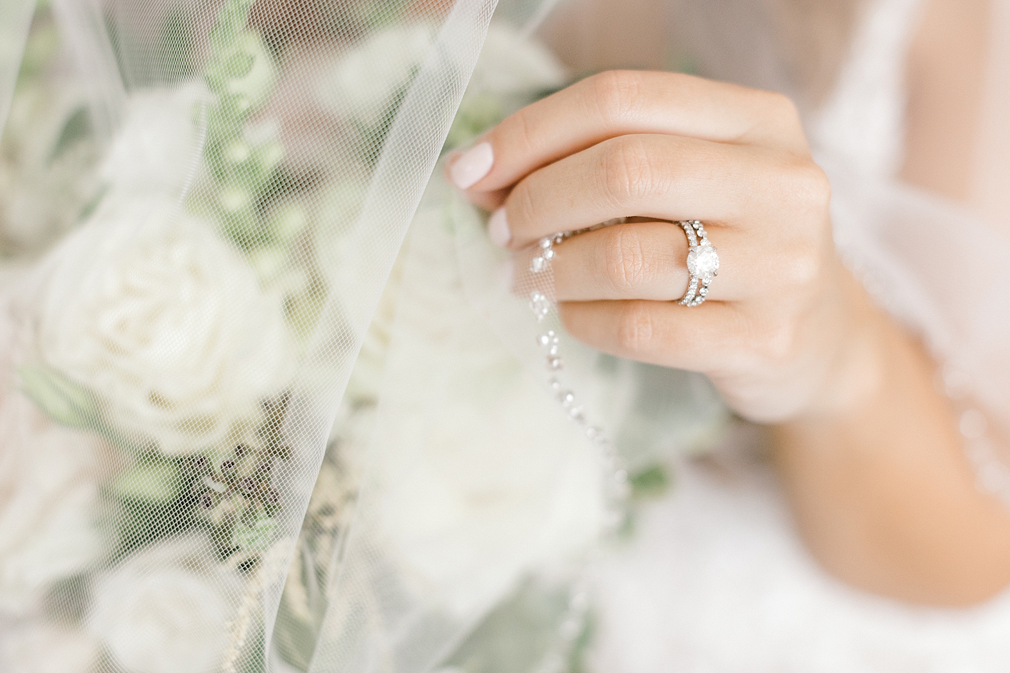 bride holds veil around bouquet showing off engagement ring