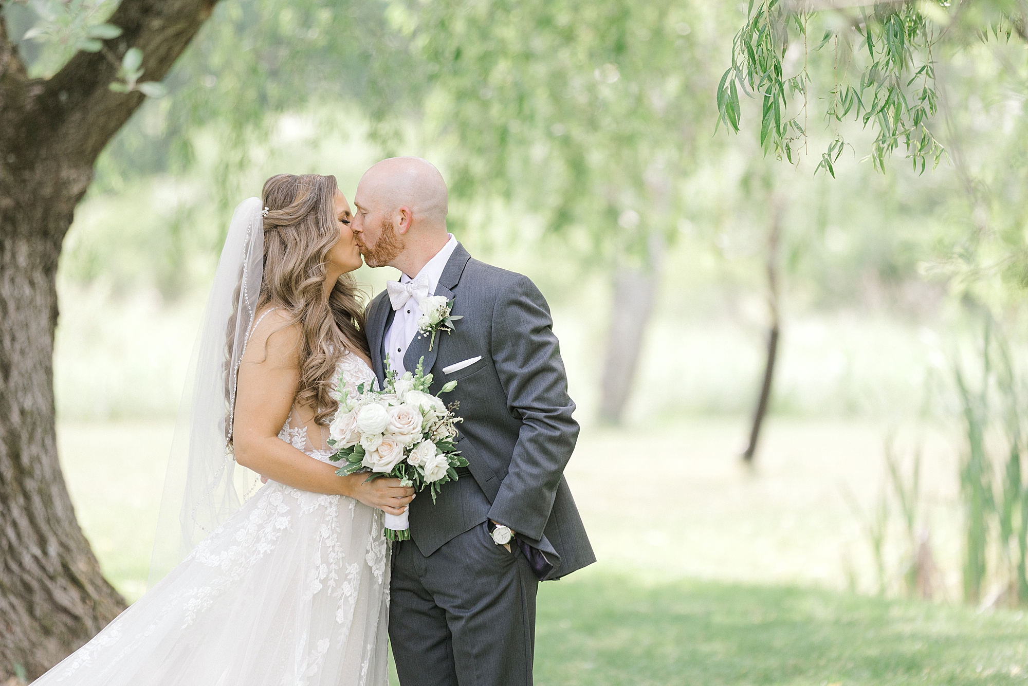 newlyweds kiss under weeping willow at the Refinery at Perona Farms