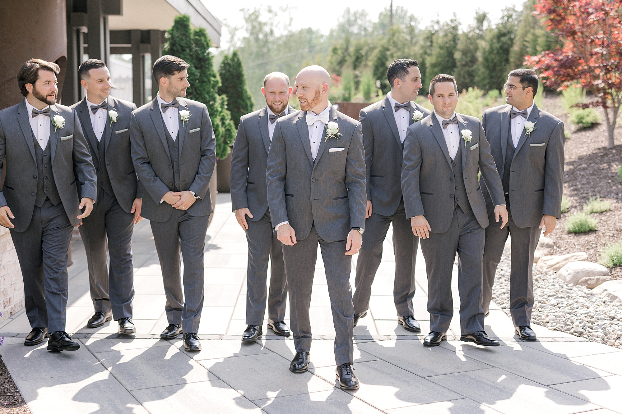 groom and groomsmen in grey suits walk outside the Refinery at Perona Farms