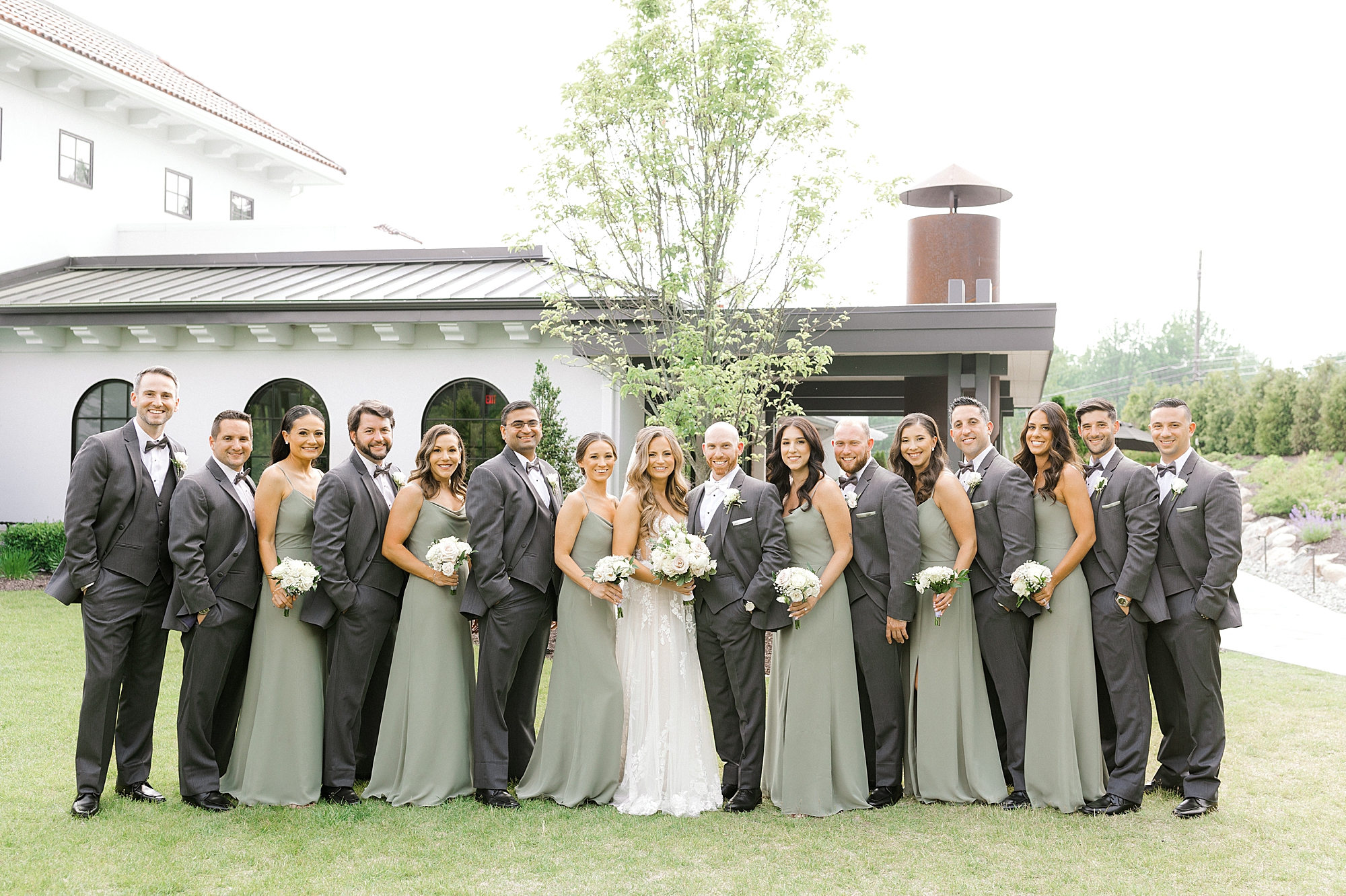 groom and bride pose with wedding party in sage green gowns and grey suits