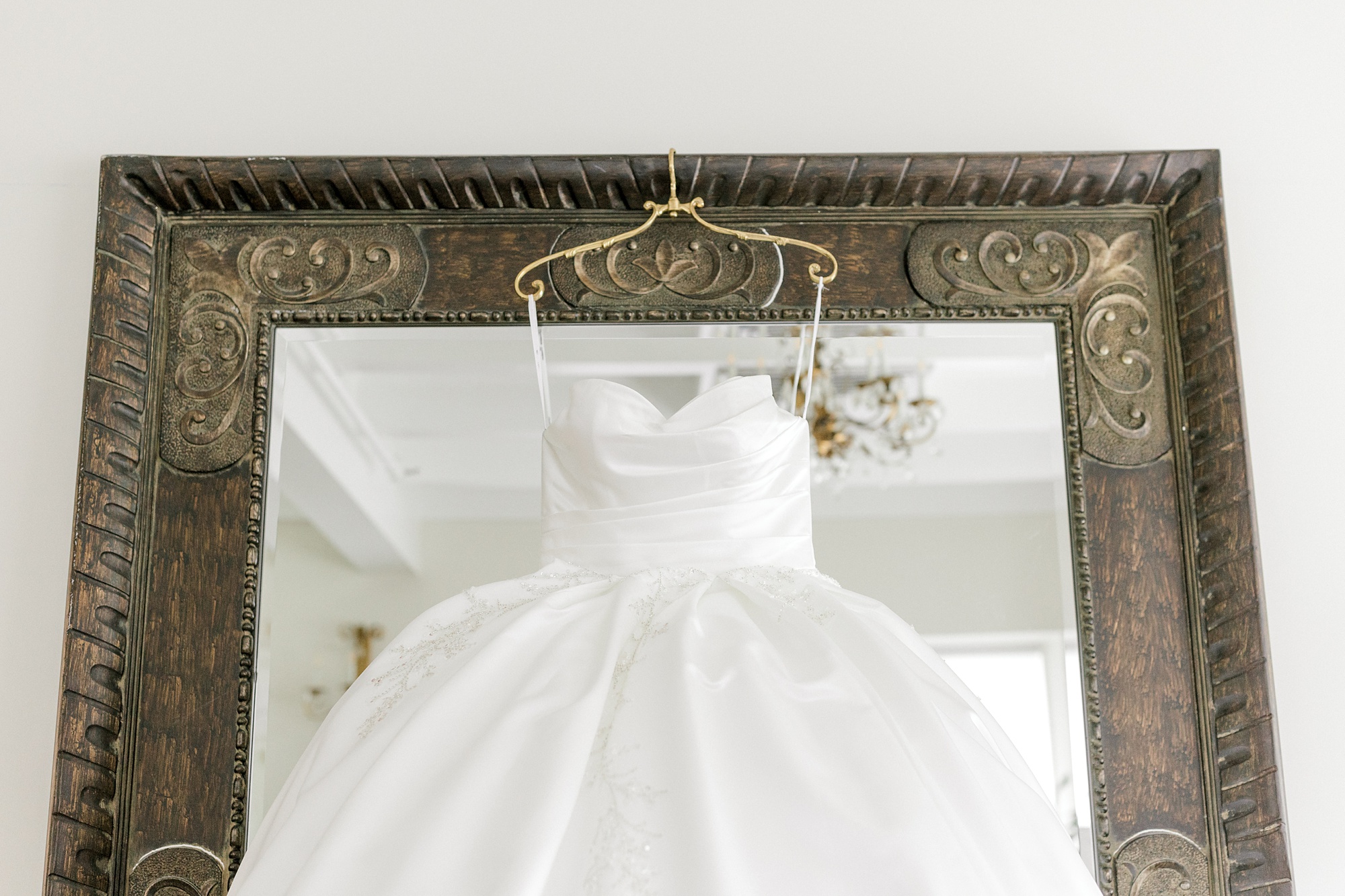 bride's dress hangs on mirror with gold frame