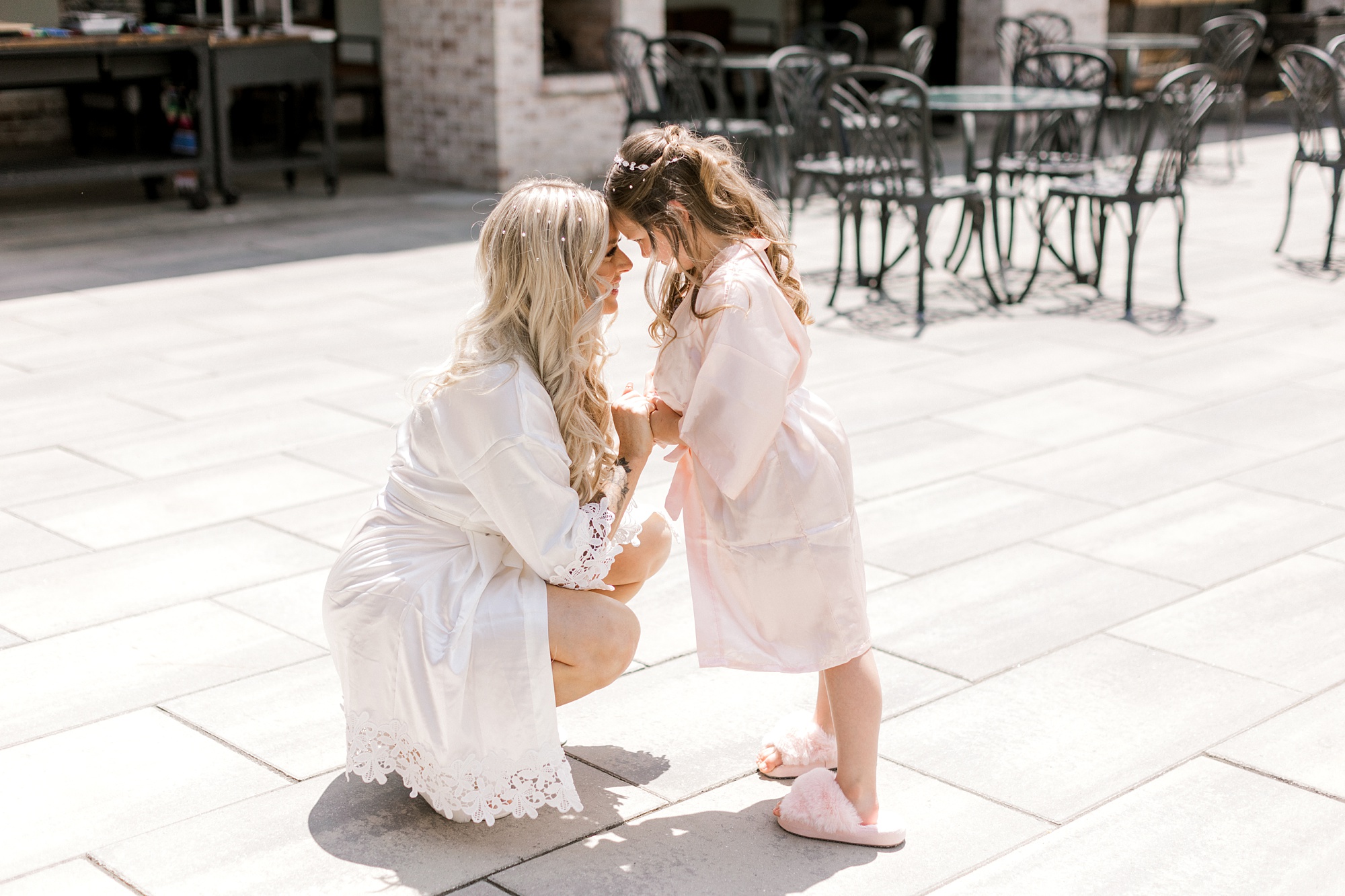 bridesmaid kneels in front of flower girl touching foreheads