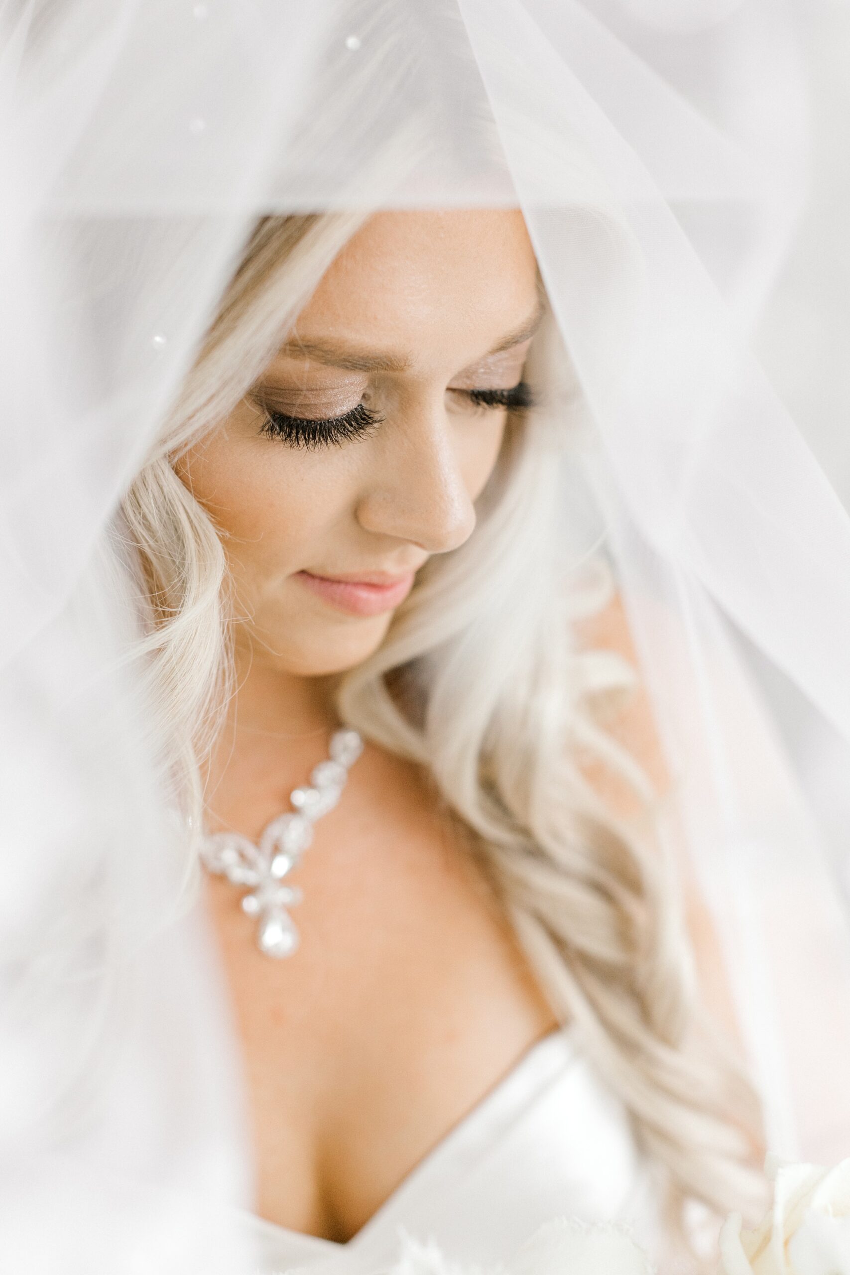 blonde bride looks down under veil with diamond necklace