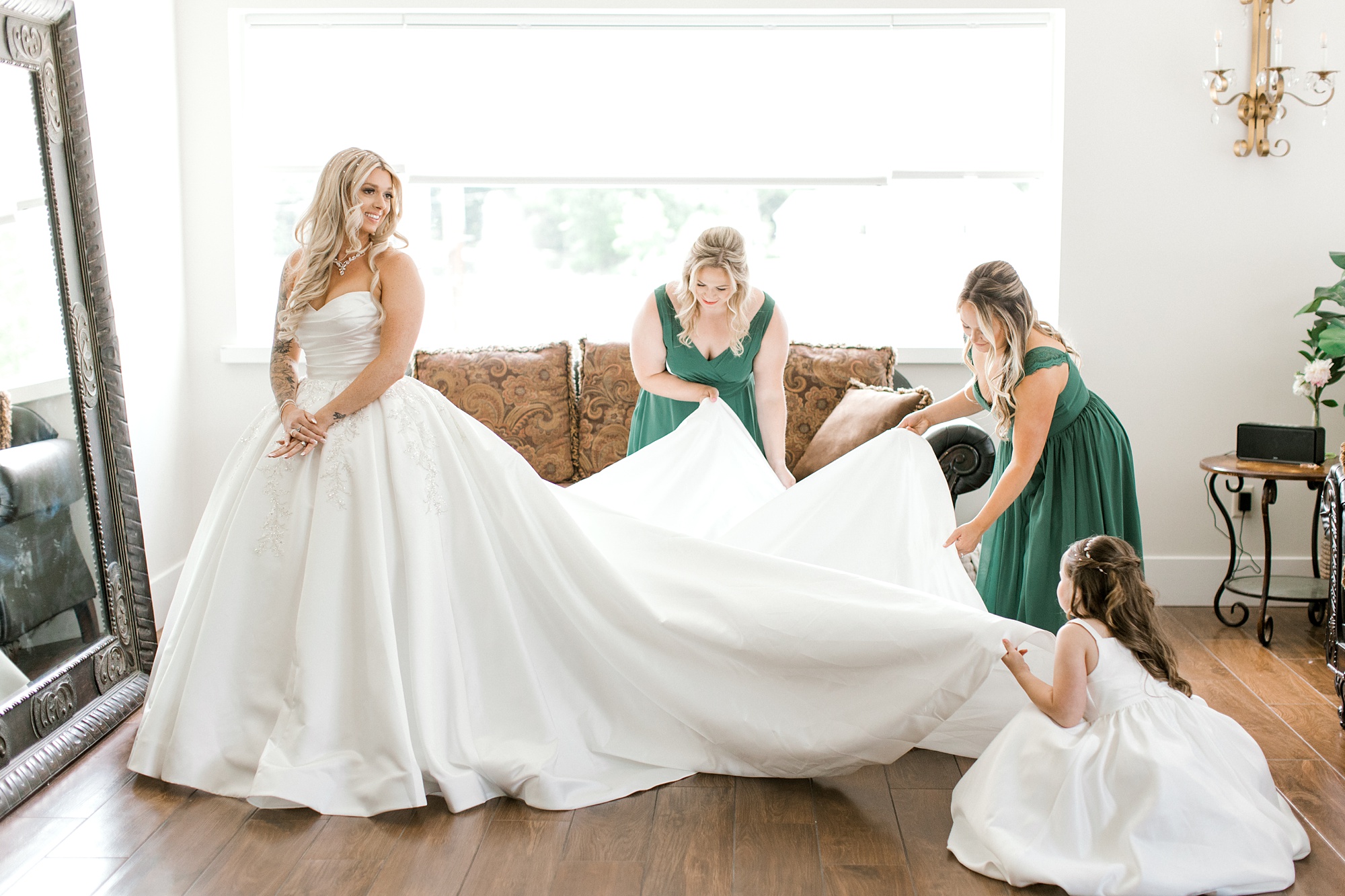 bridesmaids in green gowns pull out train on bride's wedding dress