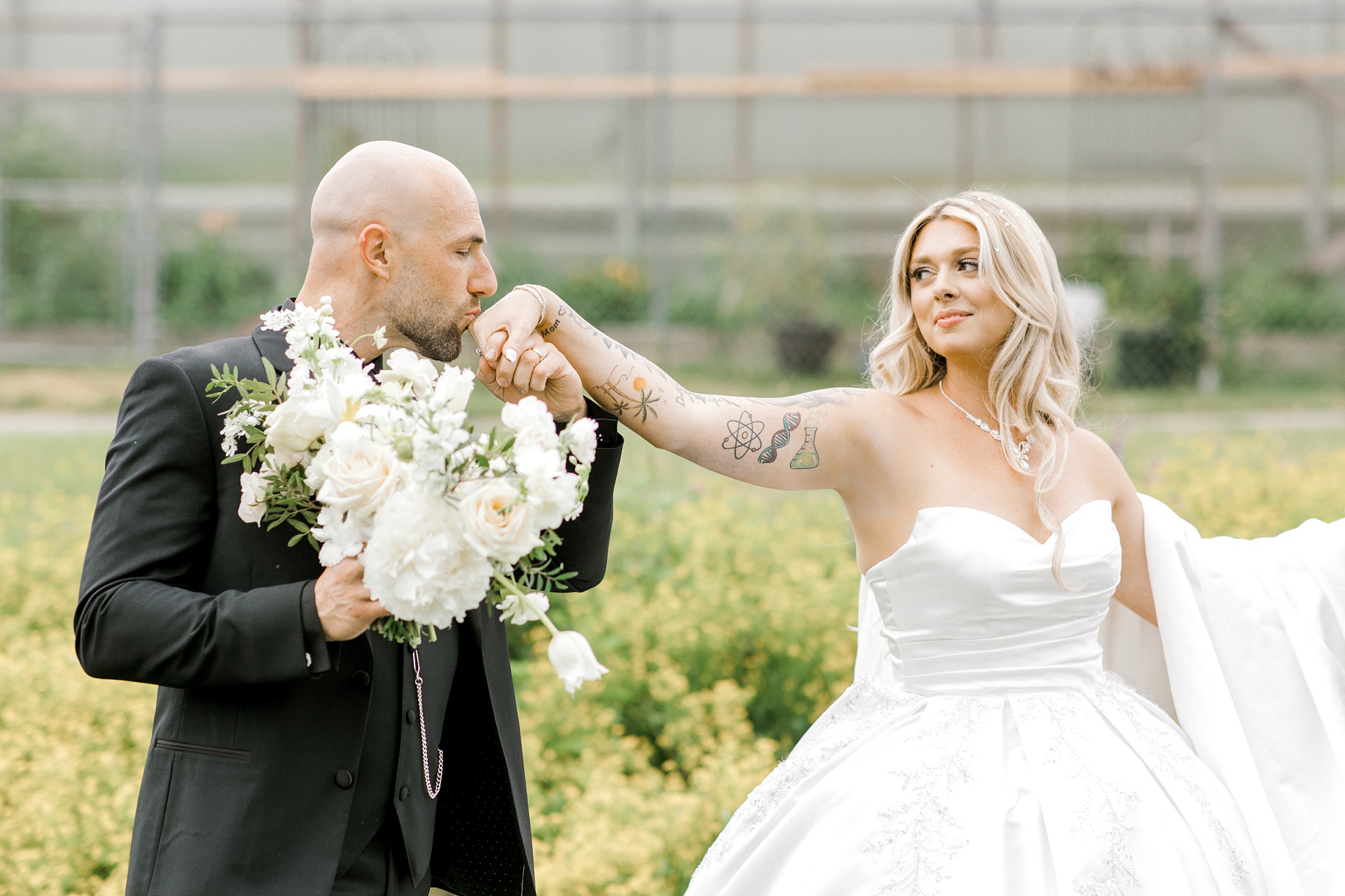 groom kisses bride's hand outside greenhouse at the Refinery at Perona Farms