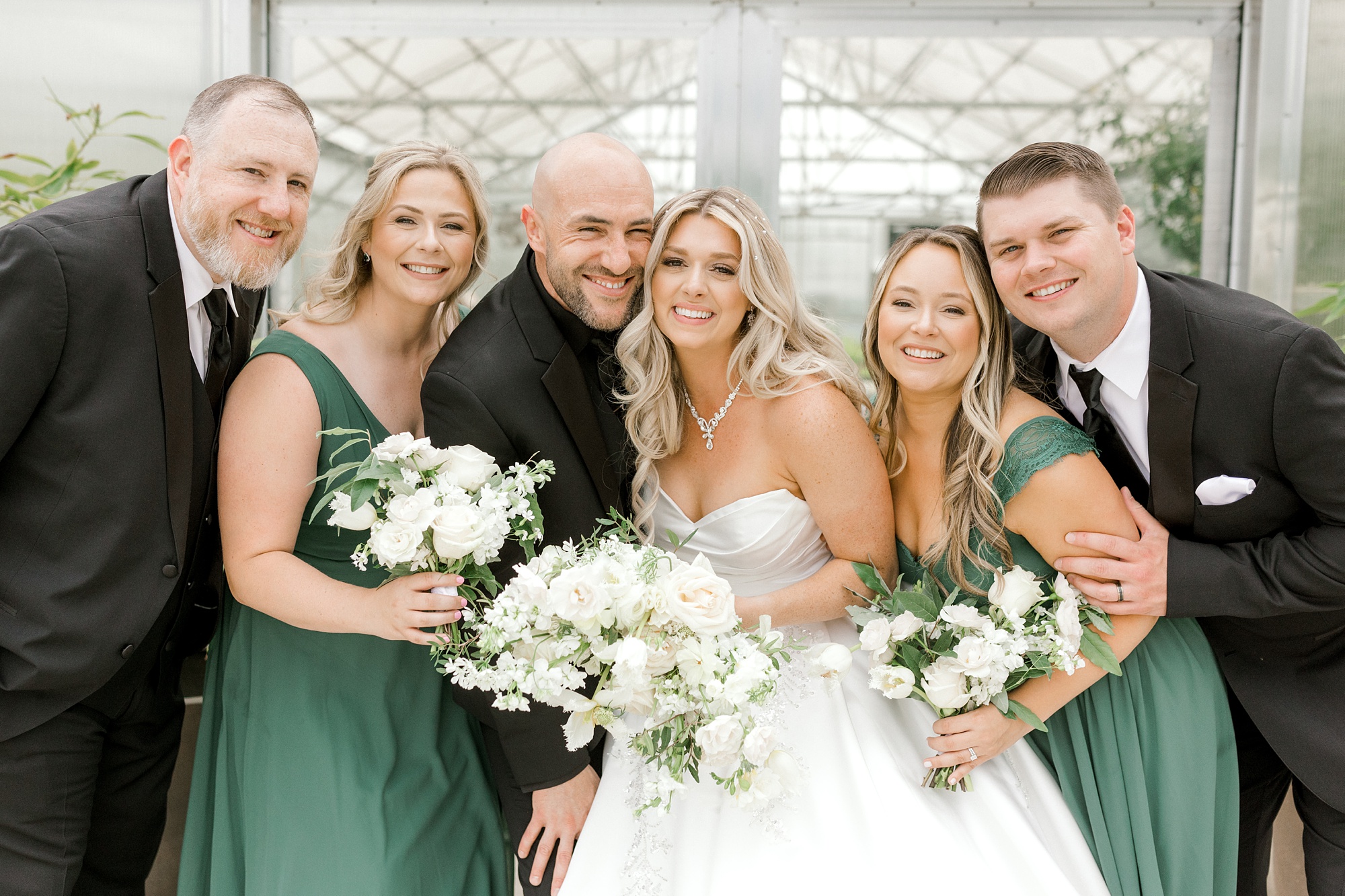 newlyweds smile with wedding party in black and green at the Refinery at Perona Farms