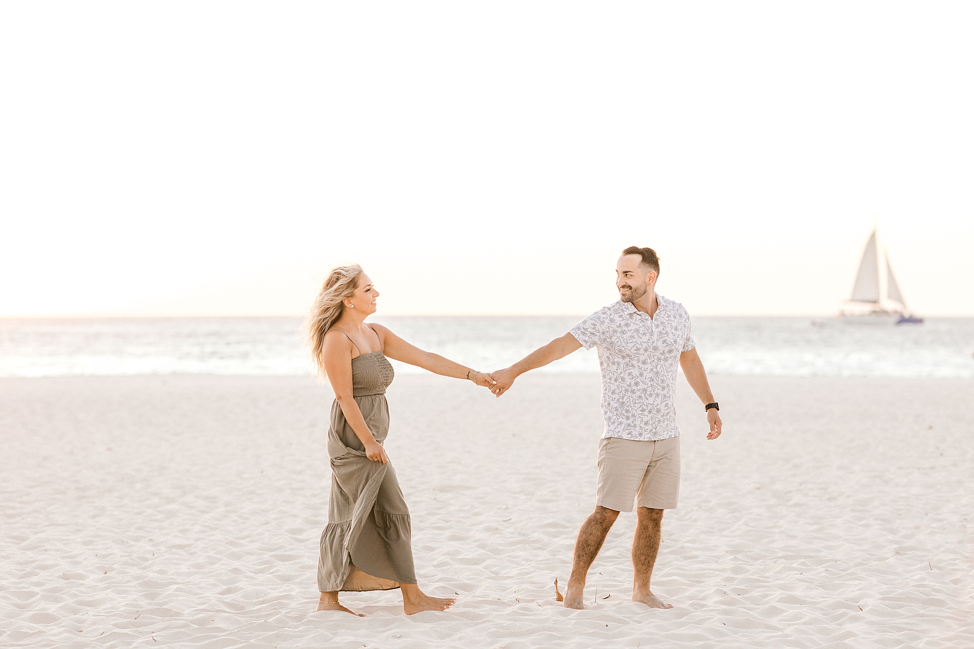 couple holds hands walking across sand near the water at the Bucati & Tara Beach Resort