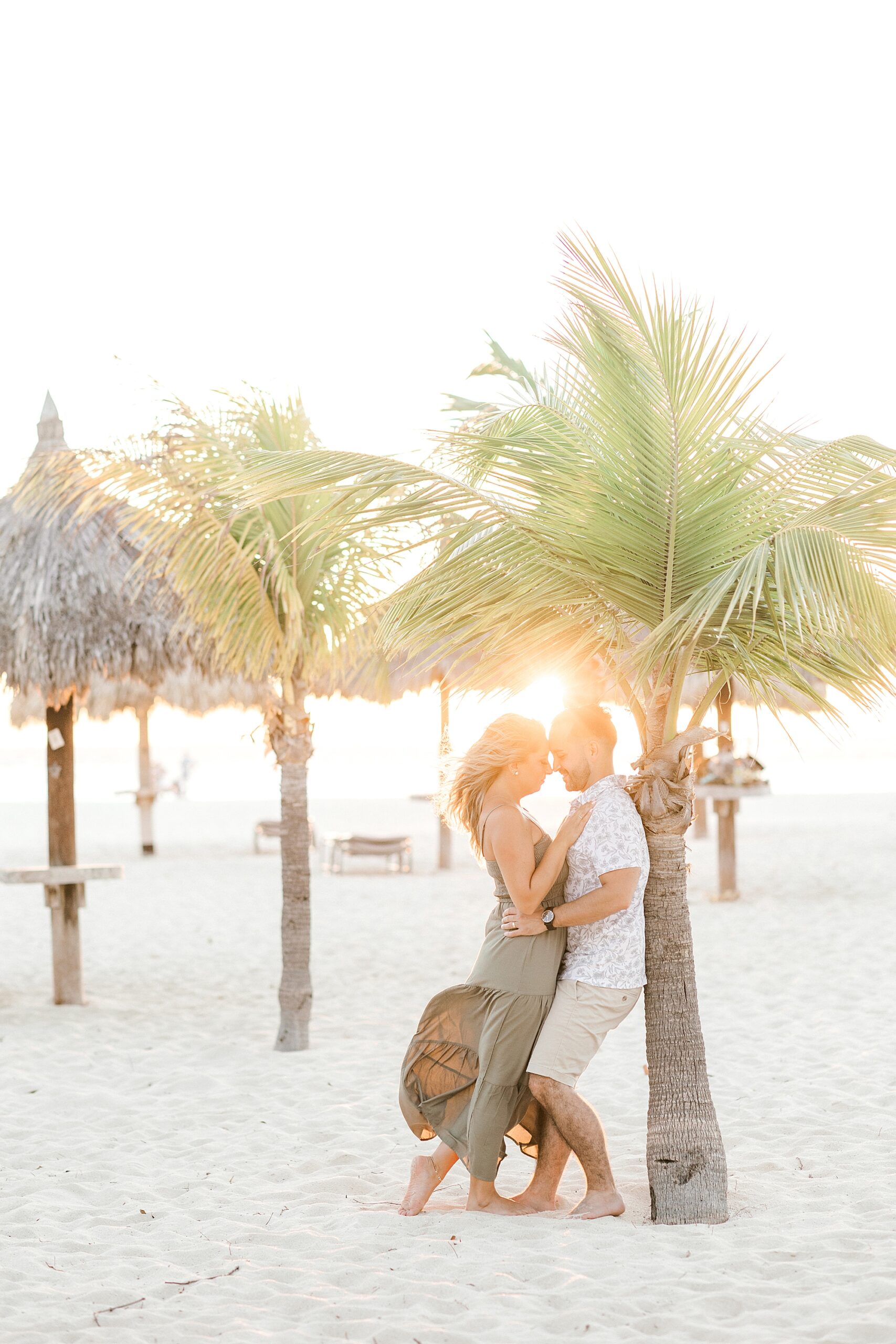 man hugs wife to him leaning against palm tree on beach at the Bucati & Tara Beach Resort