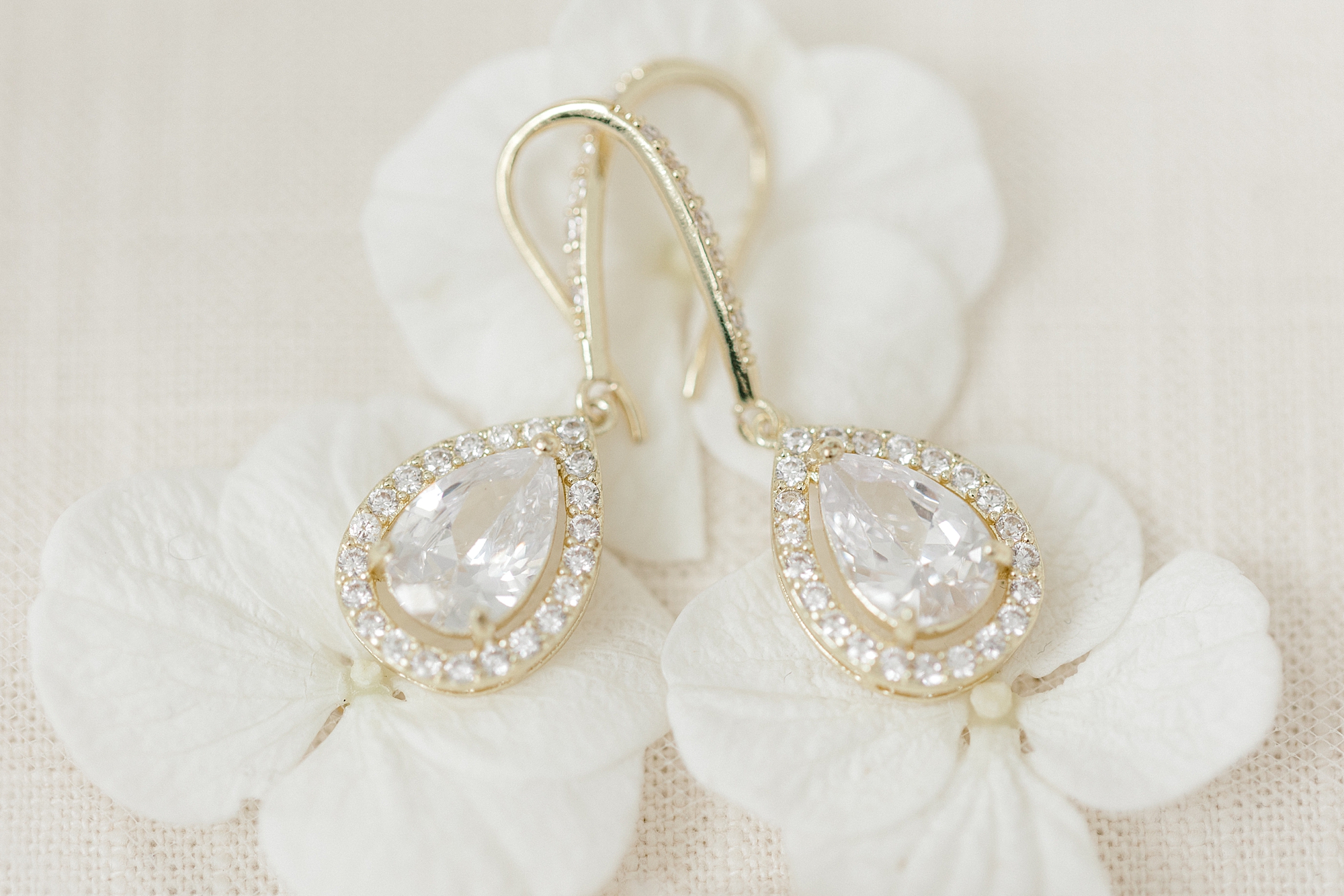 diamond earrings in gold setting lay on white flowers