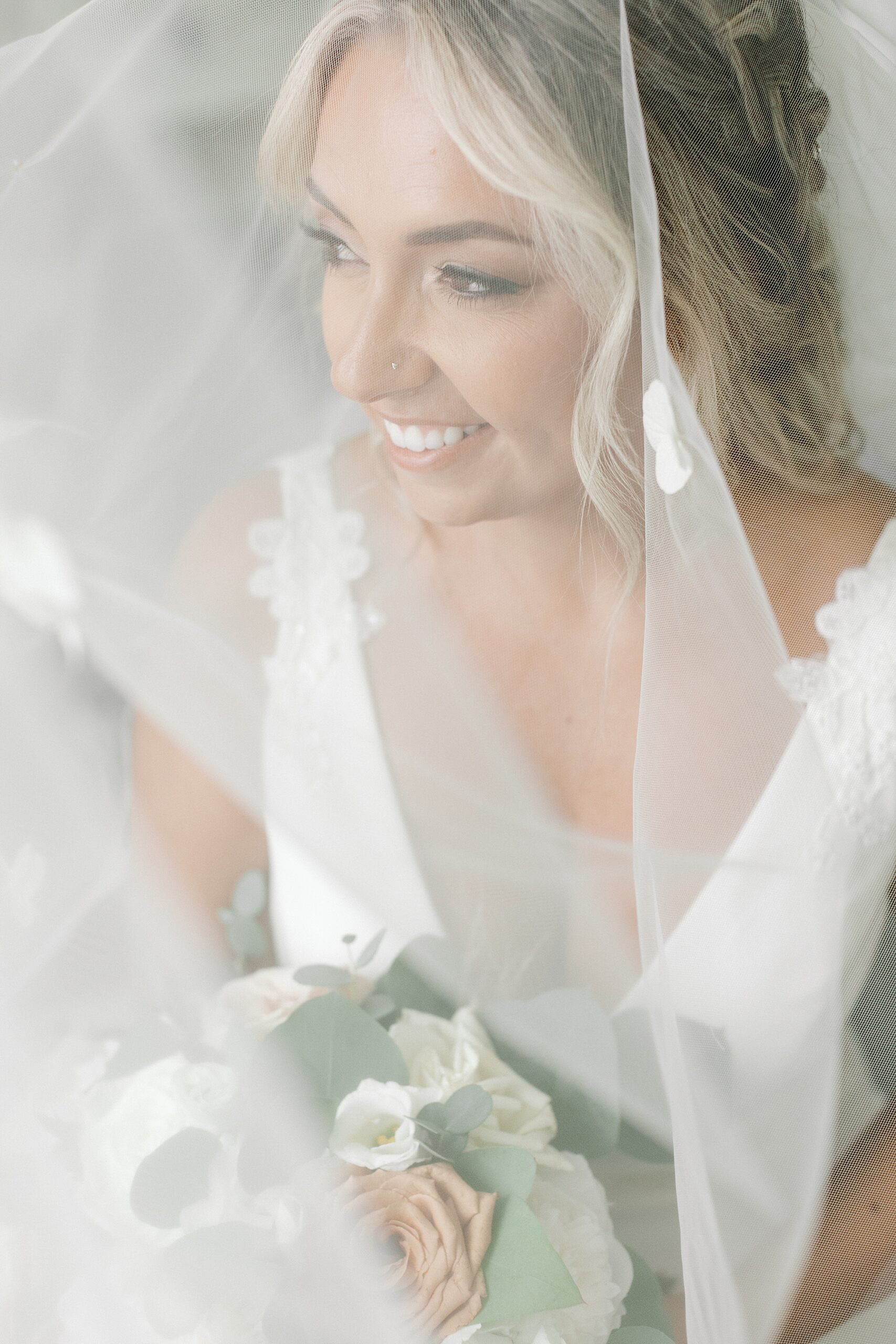 bridesmaid smiles under veil during portraits in bridal suite at the Mansion at Mountain Lakes