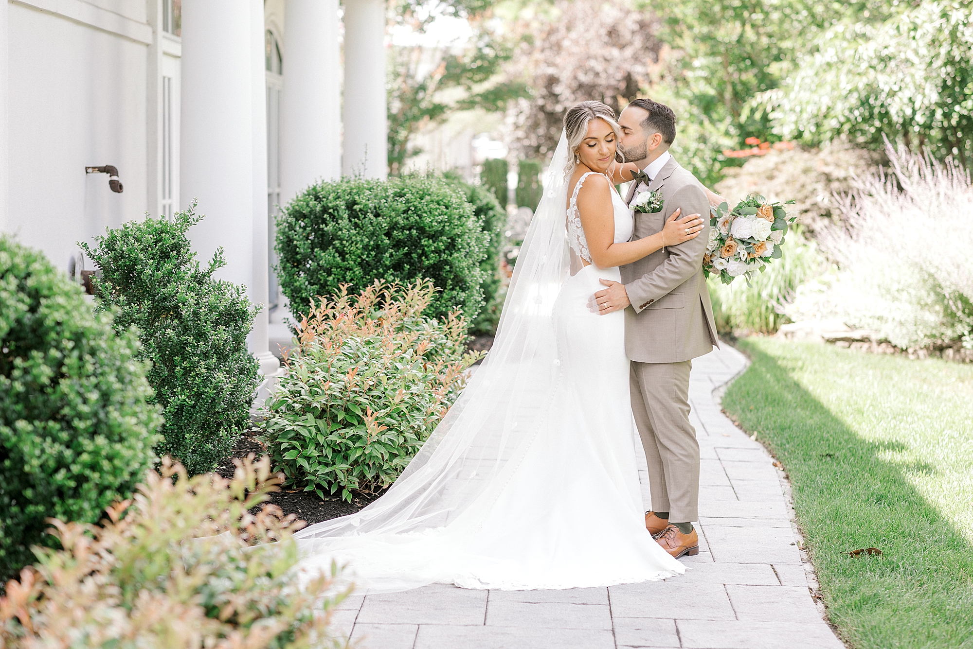 groom kisses bride's cheek on sidewalk at the Mansion at Mountain Lakes