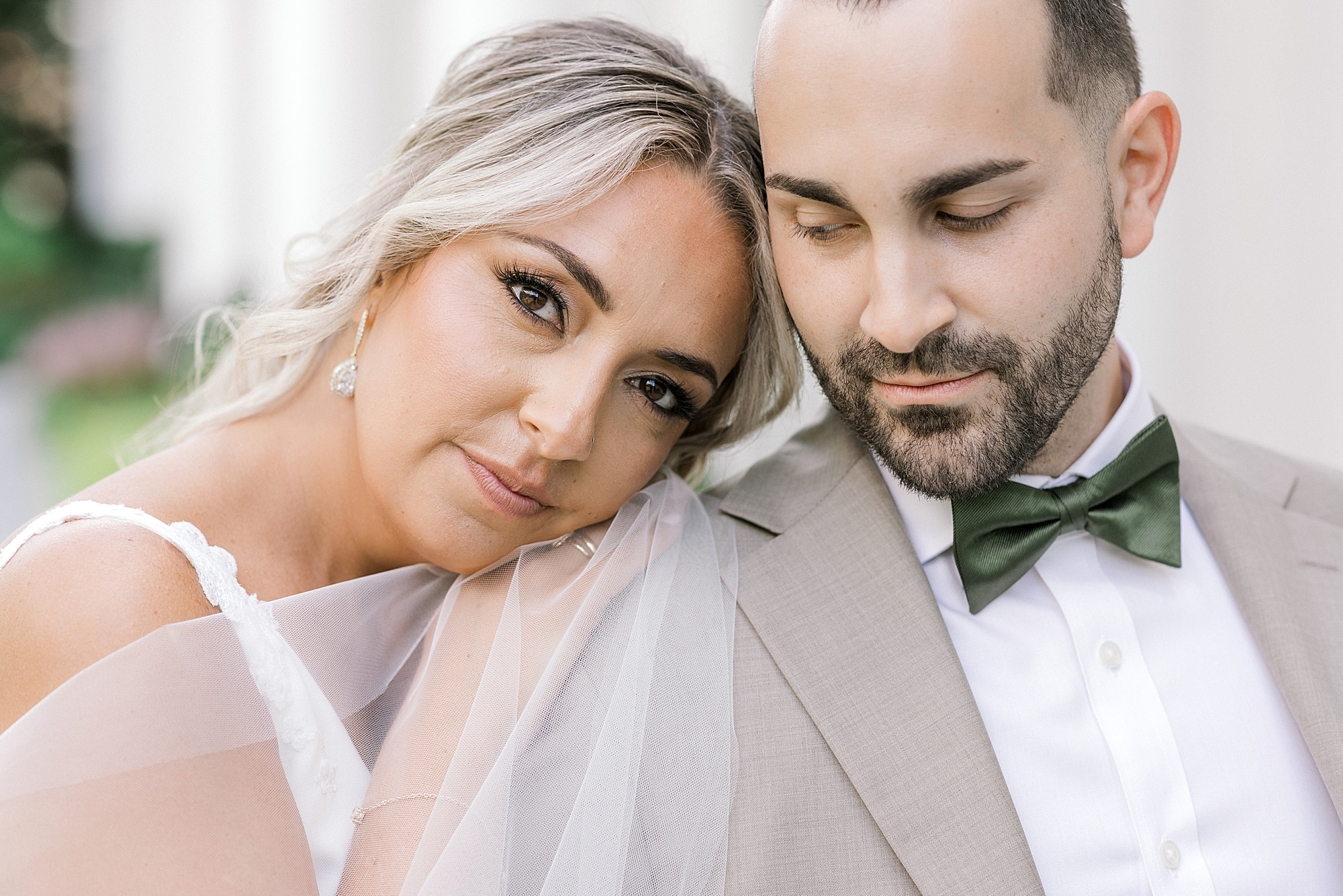 blonde bride leans head on groom's shoulder in tan suit