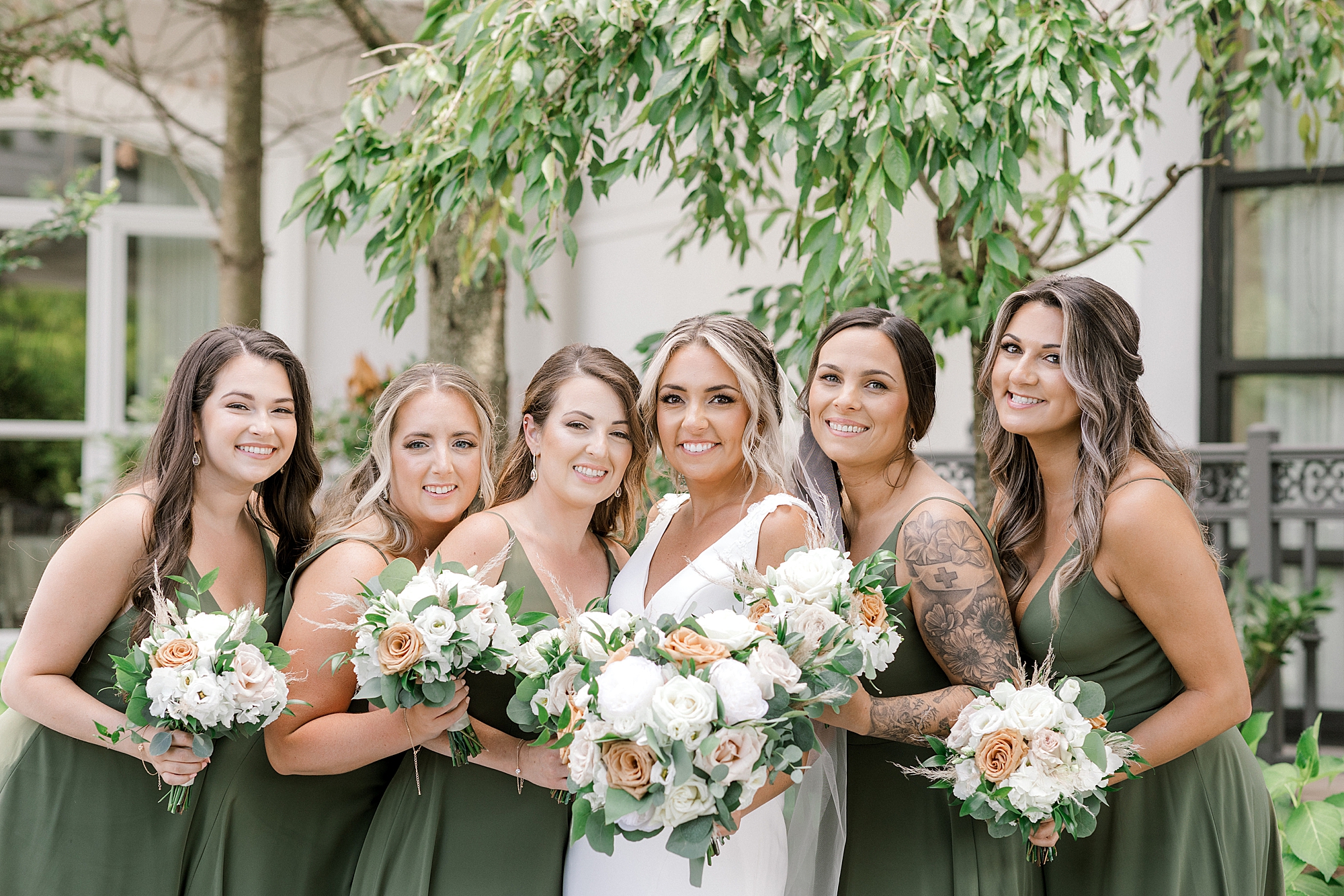 bridesmaids in green gowns hug bride in garden at the Mansion at Mountain Lakes