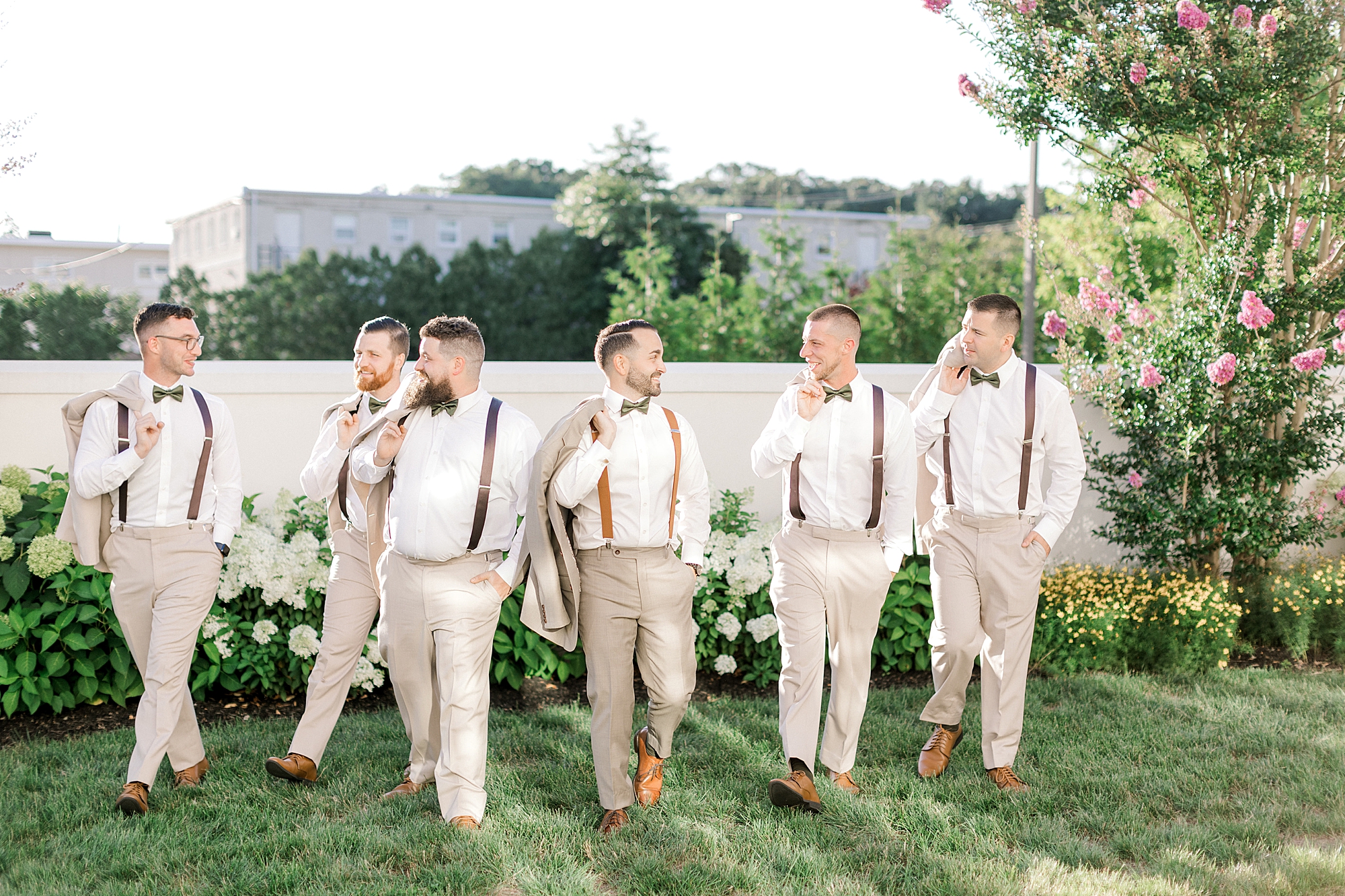 groom walks with groomsmen in suspenders on lawn at the Mansion at Mountain Lakes