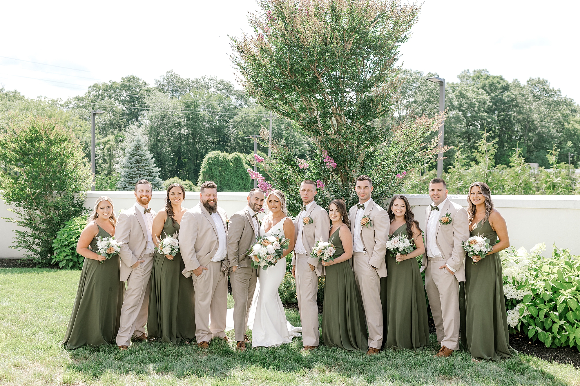 bride and groom pose with wedding party in tan and green outfits