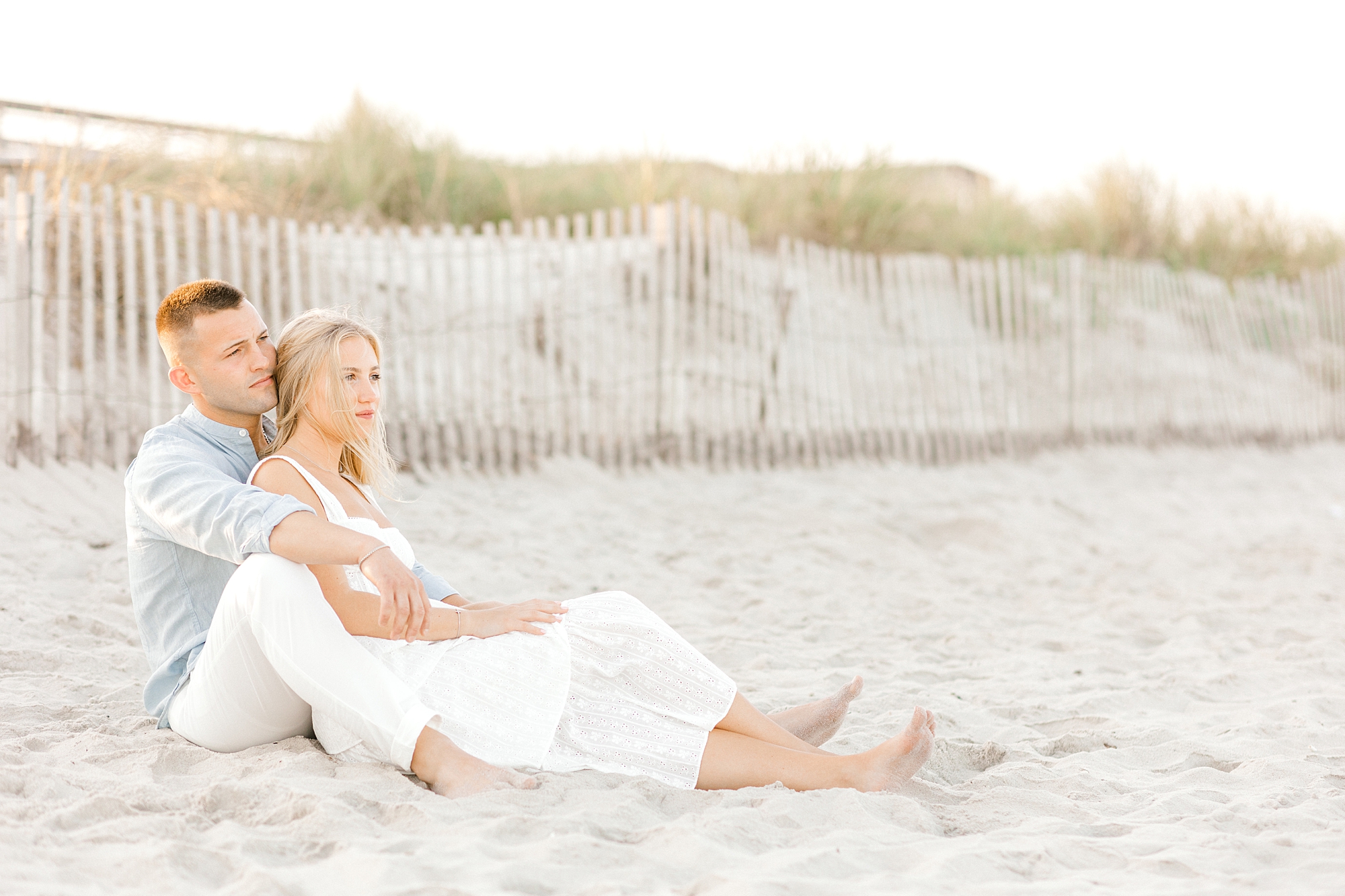 engaged couple sits together on beach during engagement session in Lavallette, NJ