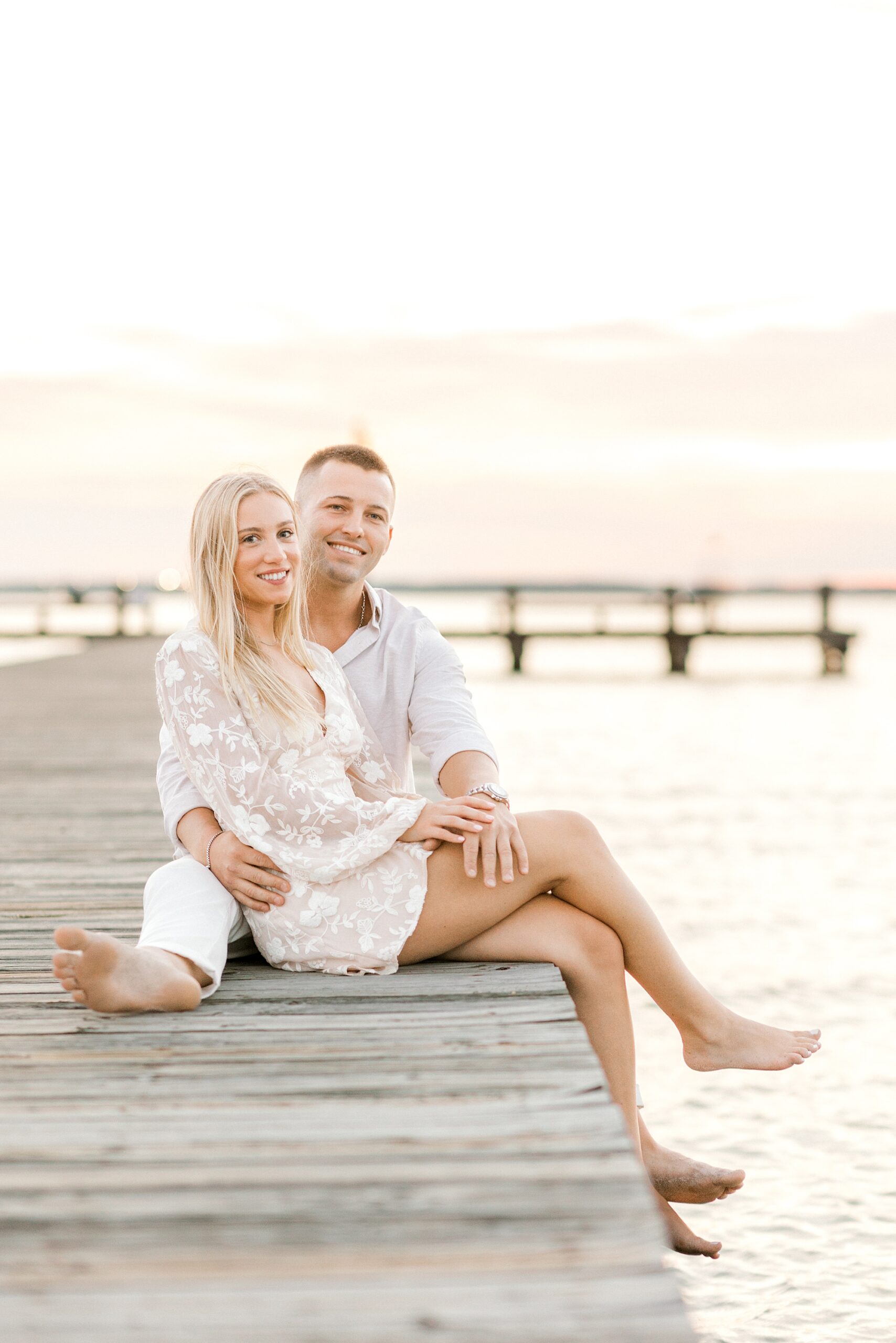 engaged couple sits on dock during NJ engagement session on the beach