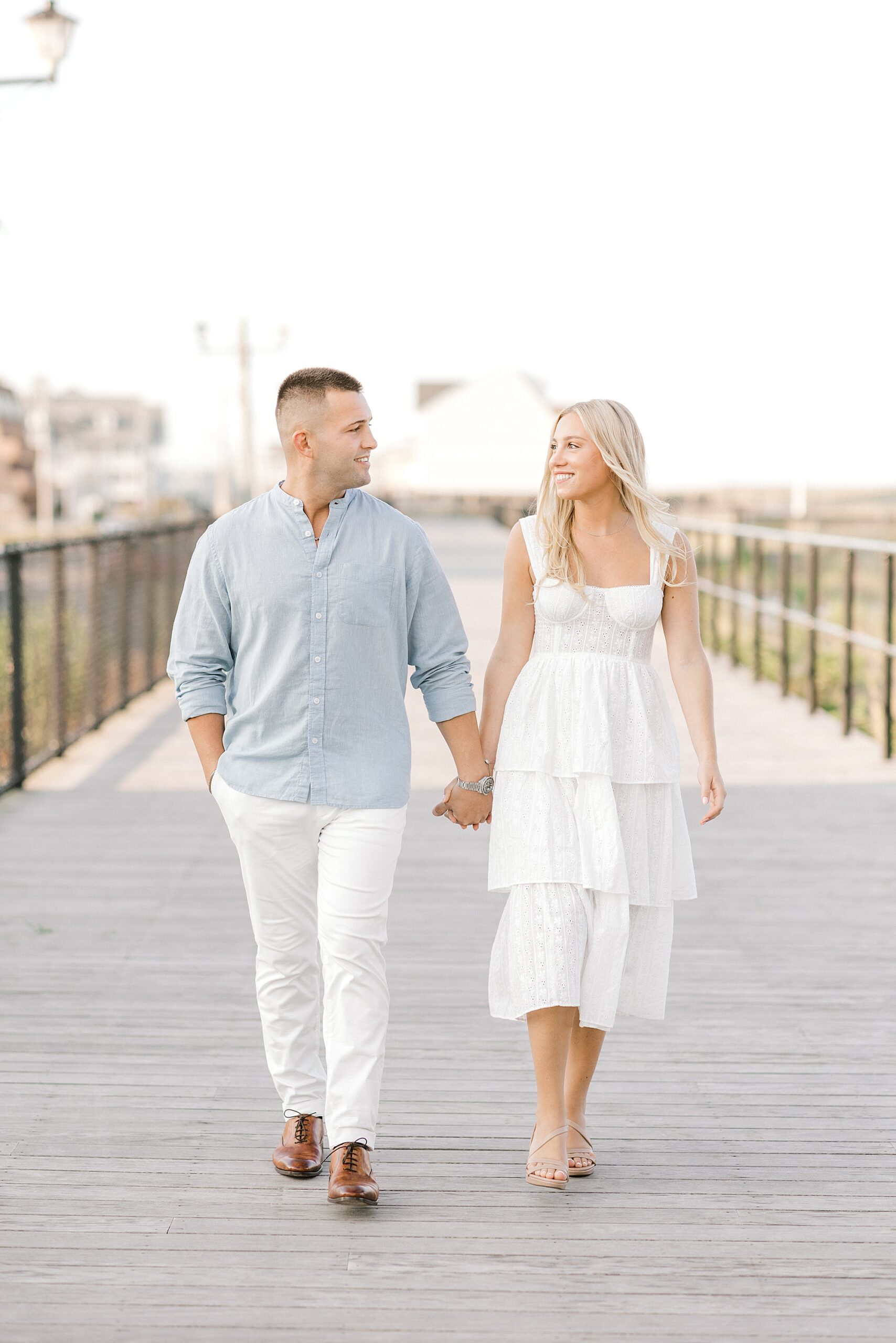 couple holds hands walking down wooden dock in Lavallette NJ