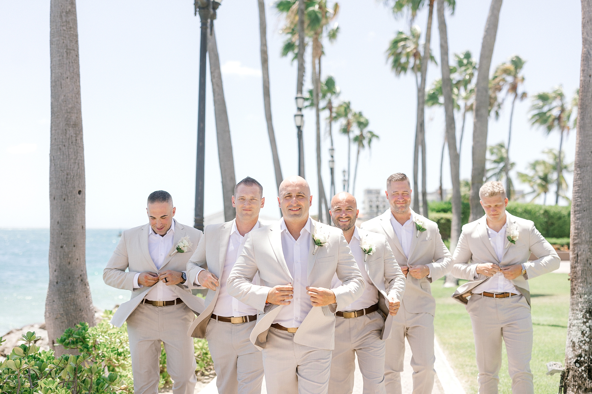 groom walks with groomsmen in tan suits in front of palm trees at the Renaissance Aruba