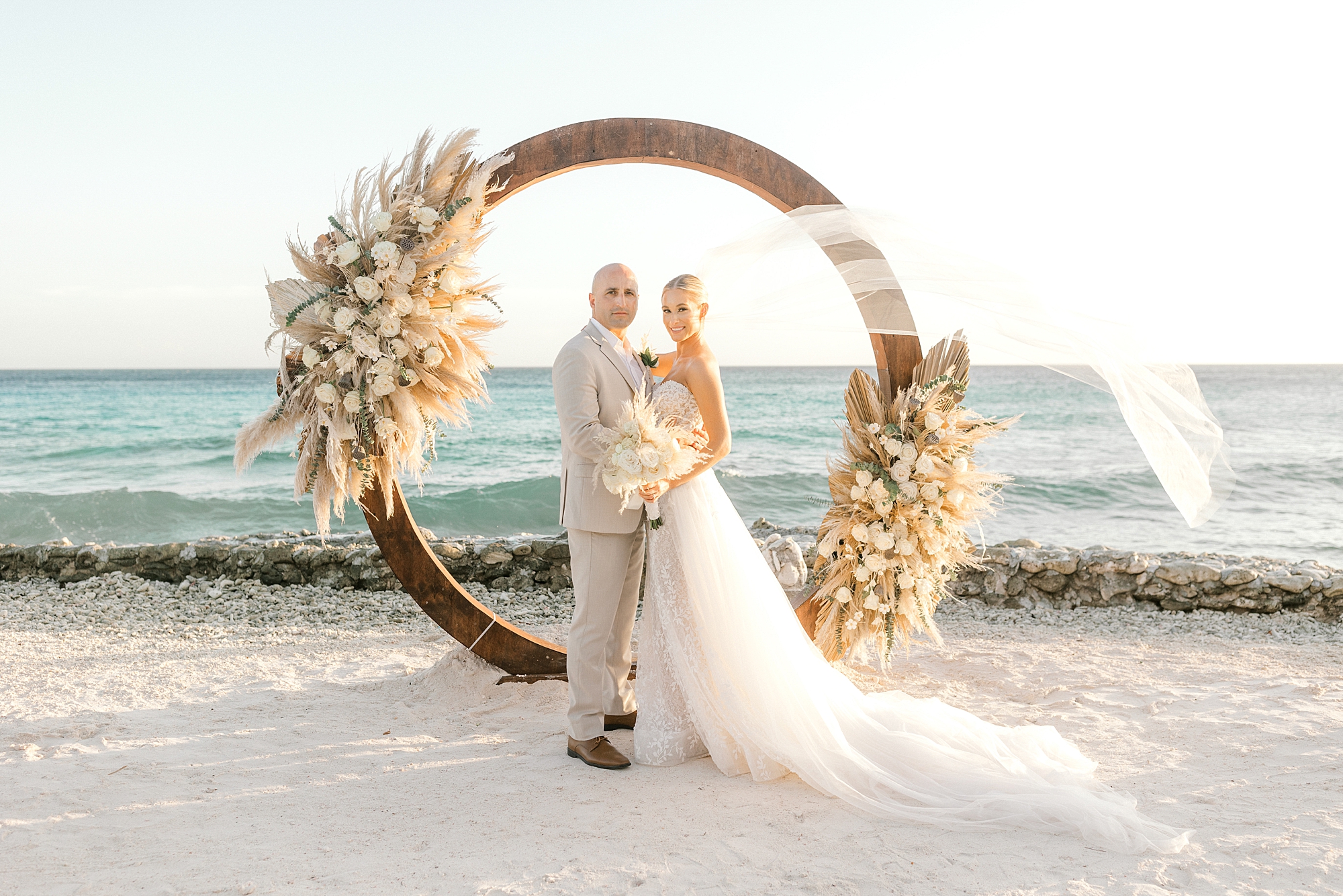 newlyweds hug in front of circular arbor on Flamingo Island with bride's veil floating in the air