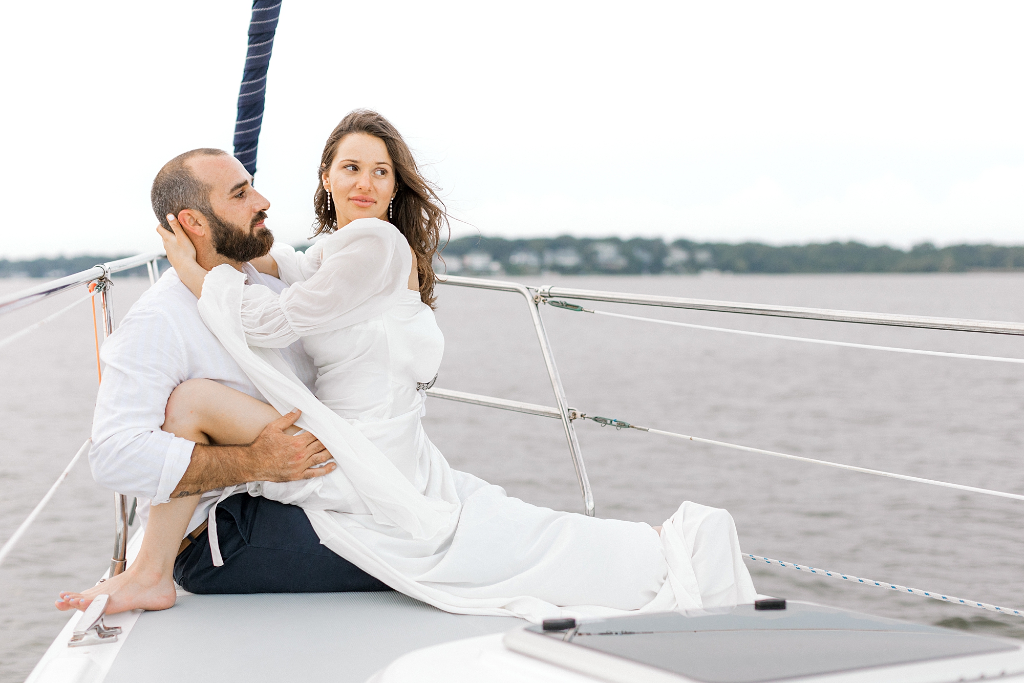 woman sits on man's lap on front of sailboat during Toms River engagement session