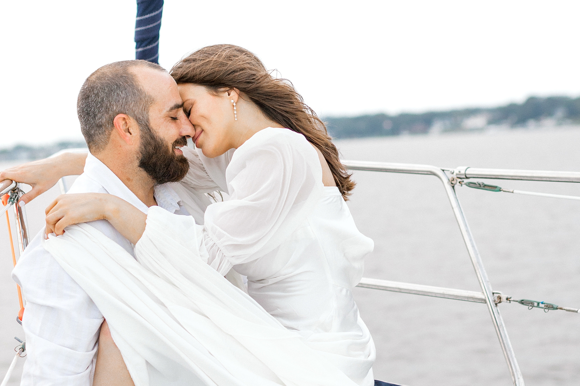 engaged couple leans to kiss on front of sailboat during Toms River engagement session