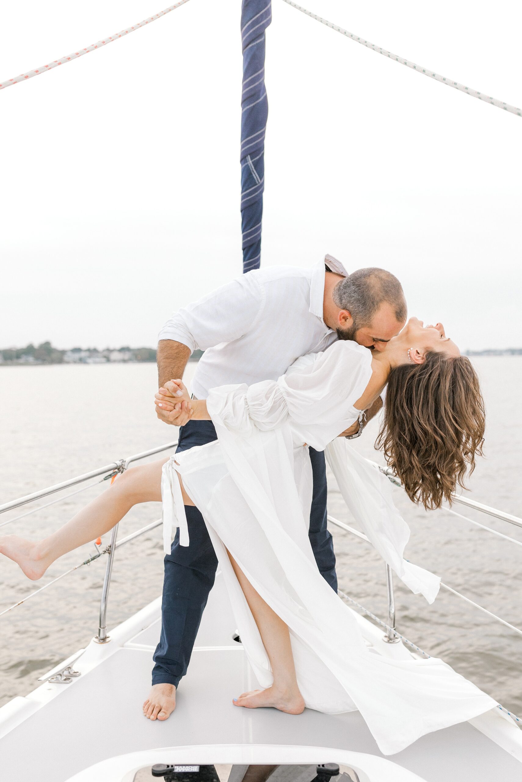 man kisses fiancee on front of sailboat while dipping her