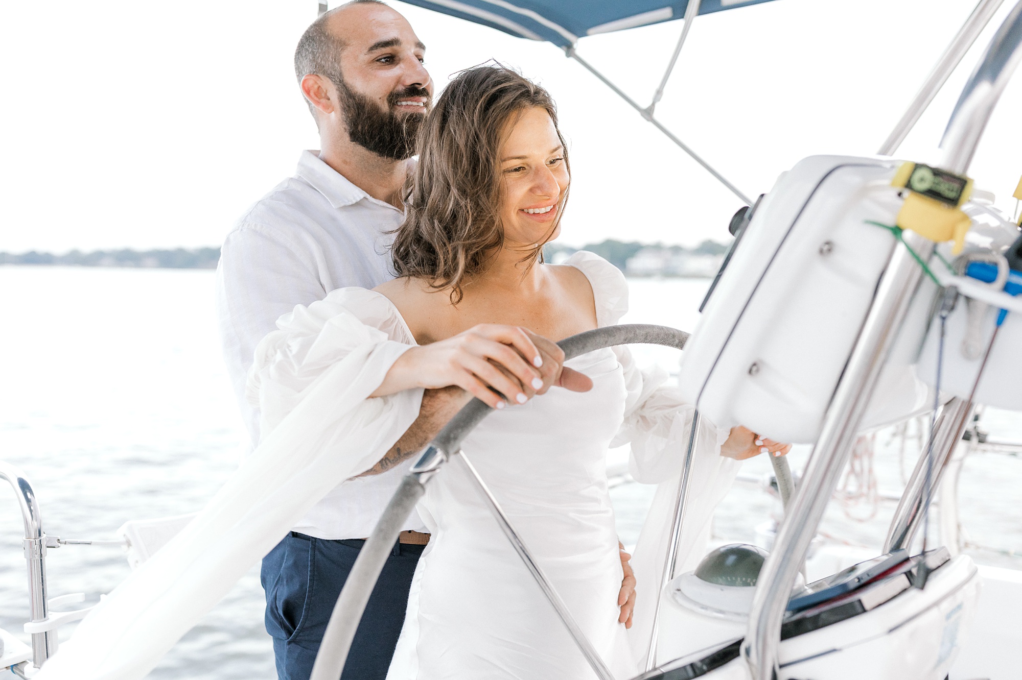 man stands behind woman steering sailboat during Toms River engagement session