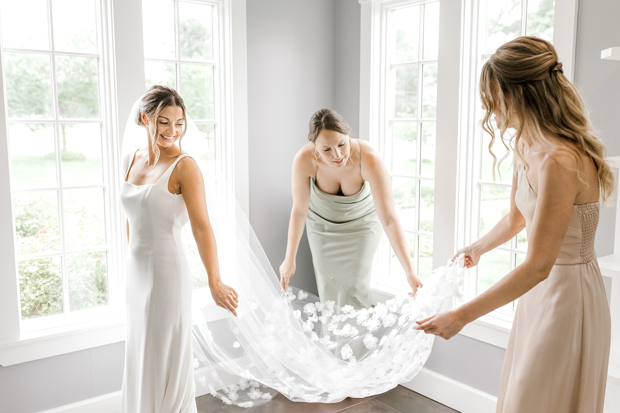 bridesmaids pull out bride's veil by windows in suite at Ryland Inn
