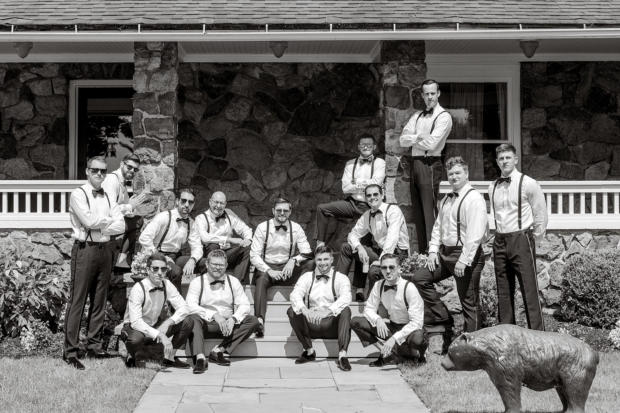 groom poses with 12 groomsmen in suspenders and bow ties on front steps of New Jersey home