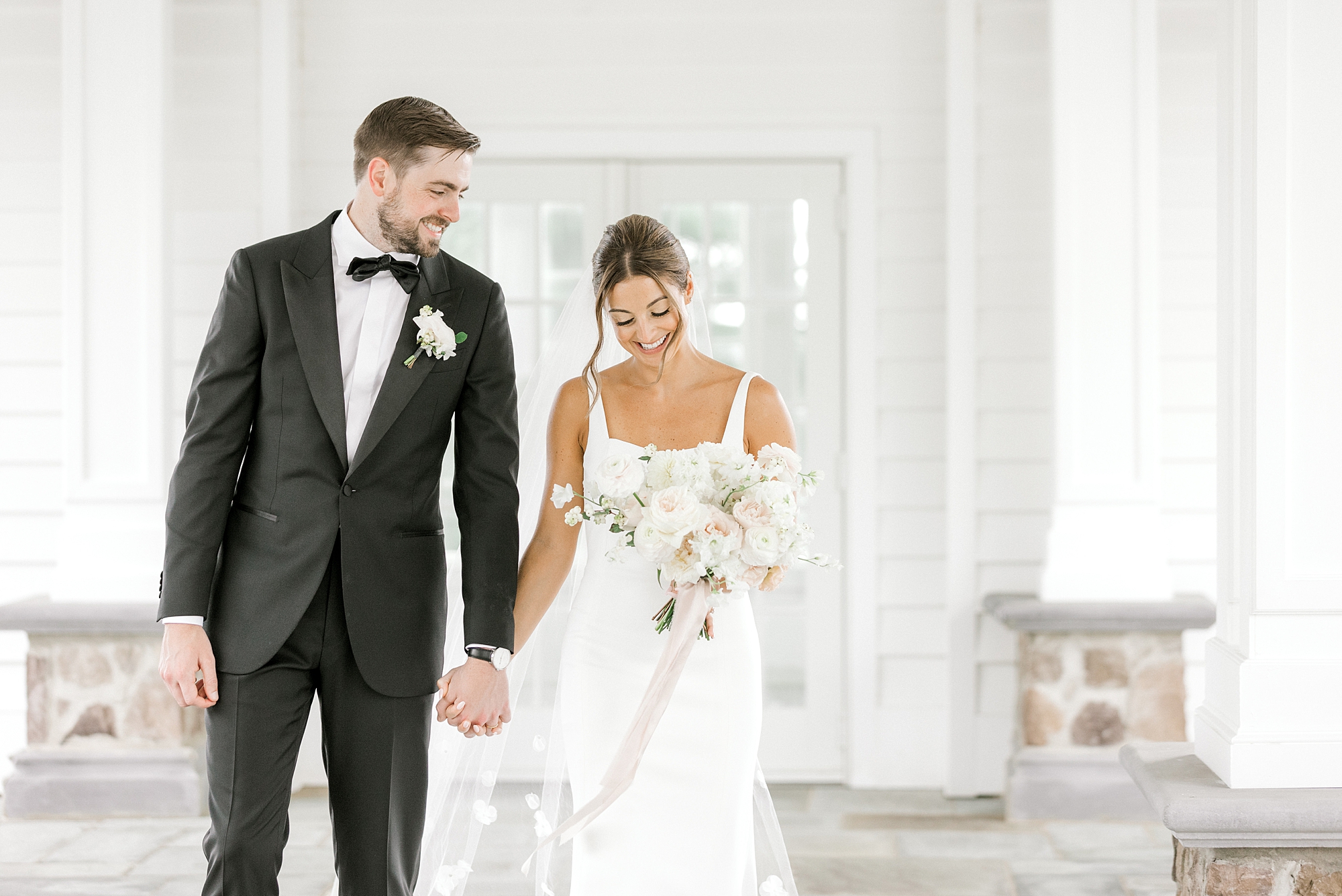 newlyweds hold hands smile and bride looks down at ground laughing