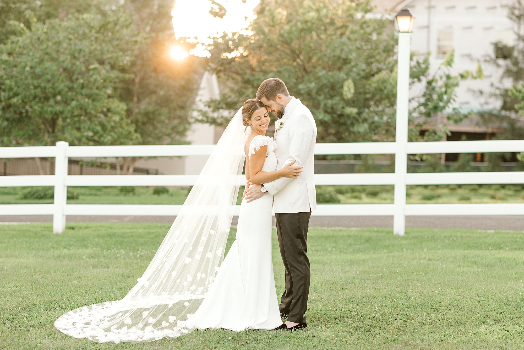 bride and groom hug at sunset in front of white fence at Ryland Inn