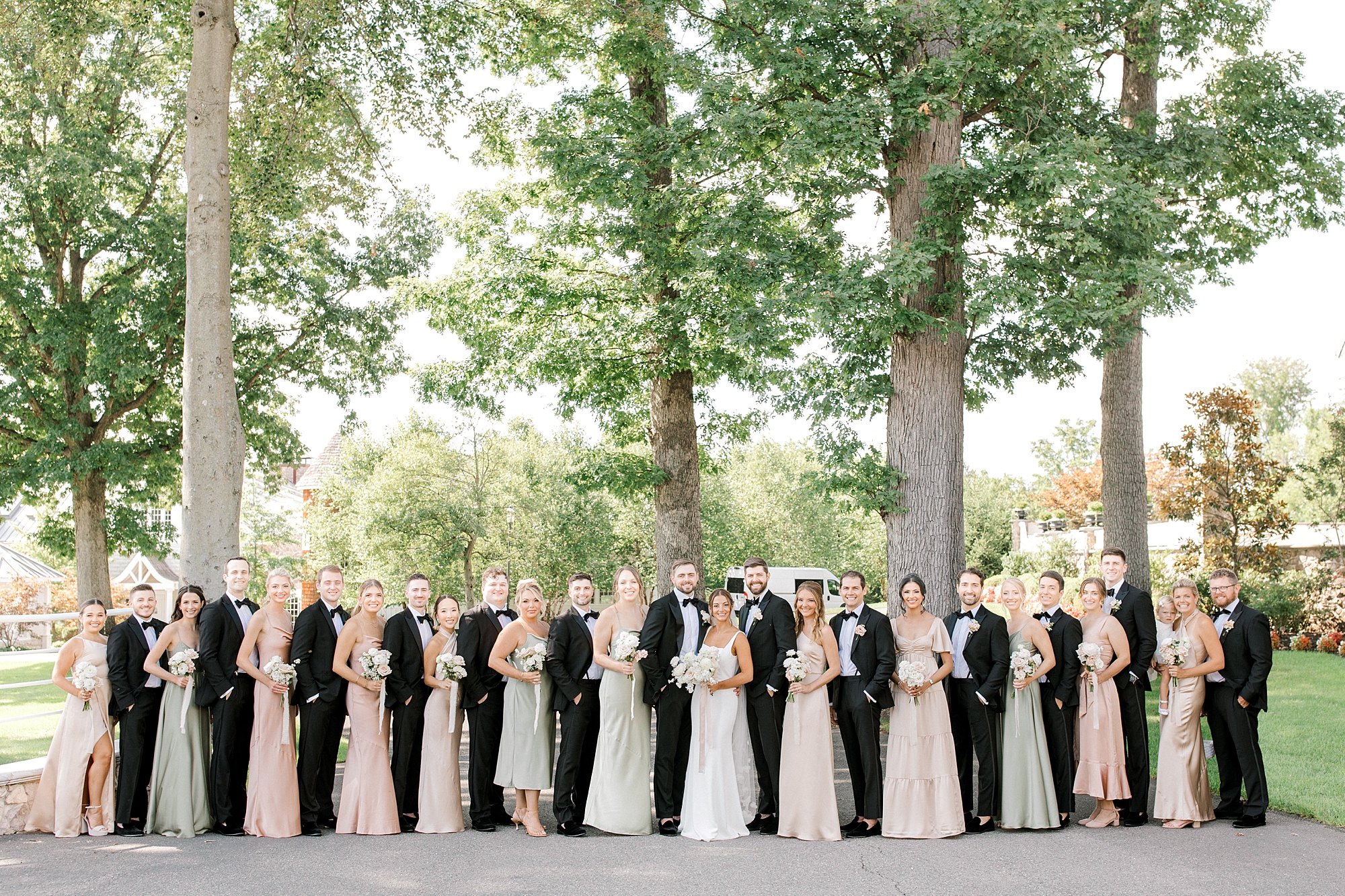 bride and groom pose with 24 person wedding party on driveway at Ryland Inn