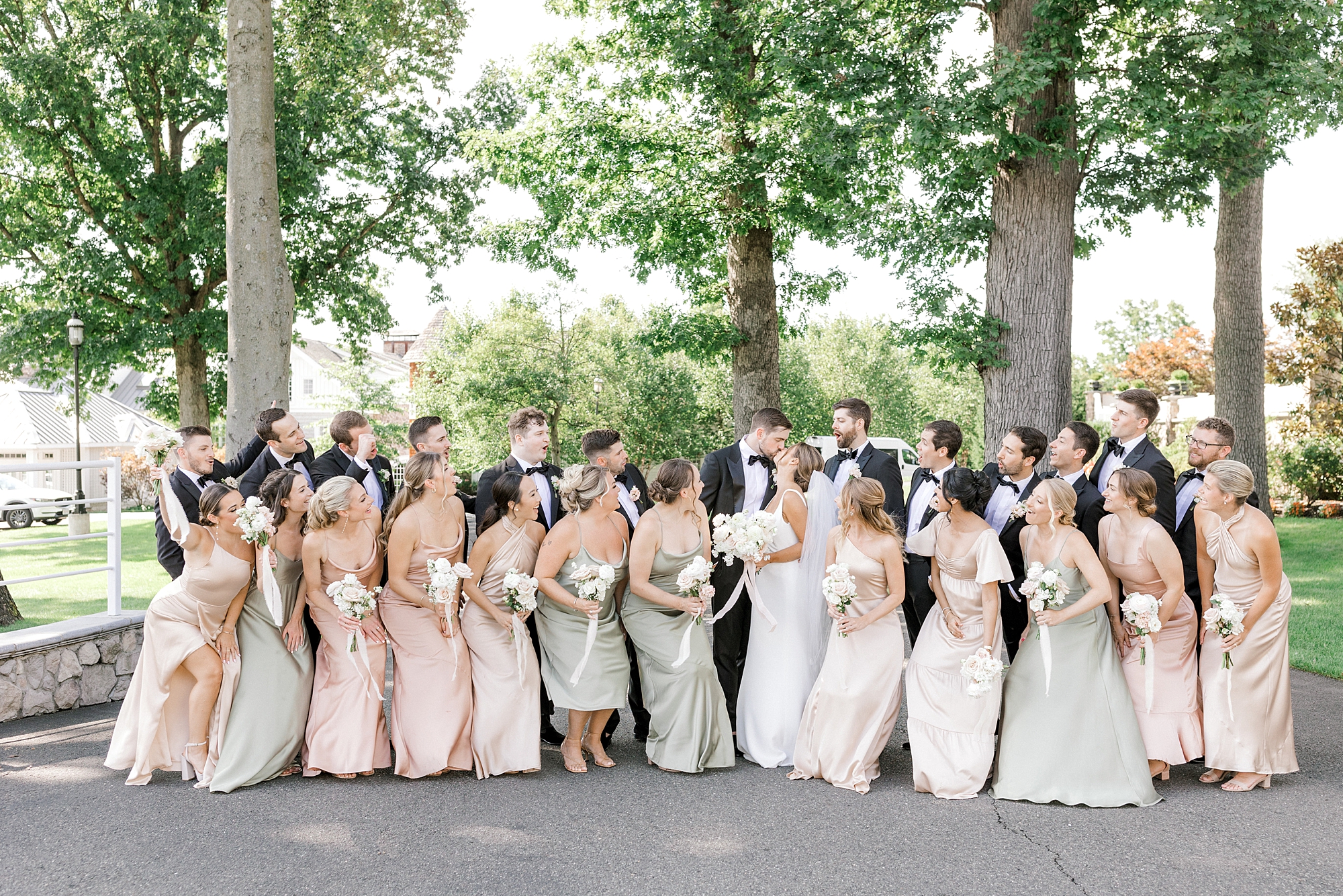 newlyweds kiss surrounded by wedding party in pink, green, and black attire